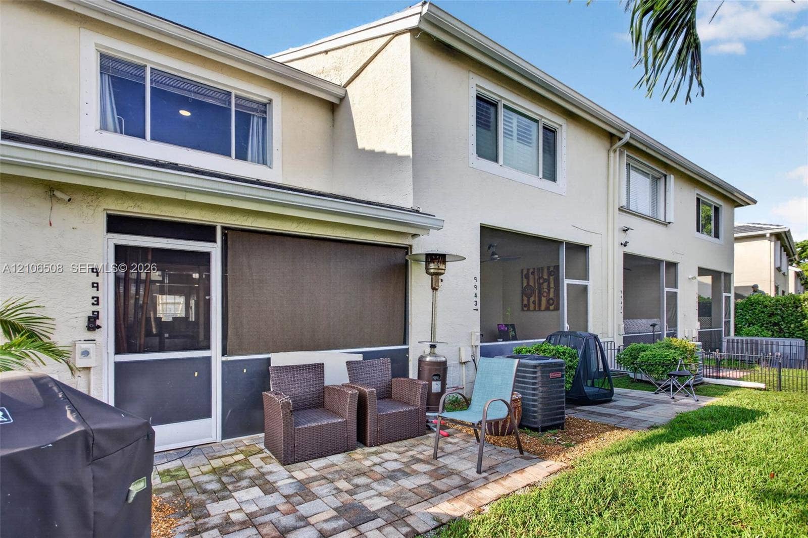 Two-story stucco exterior featuring screened-in lanais, paver patios, and sliding glass entry doors