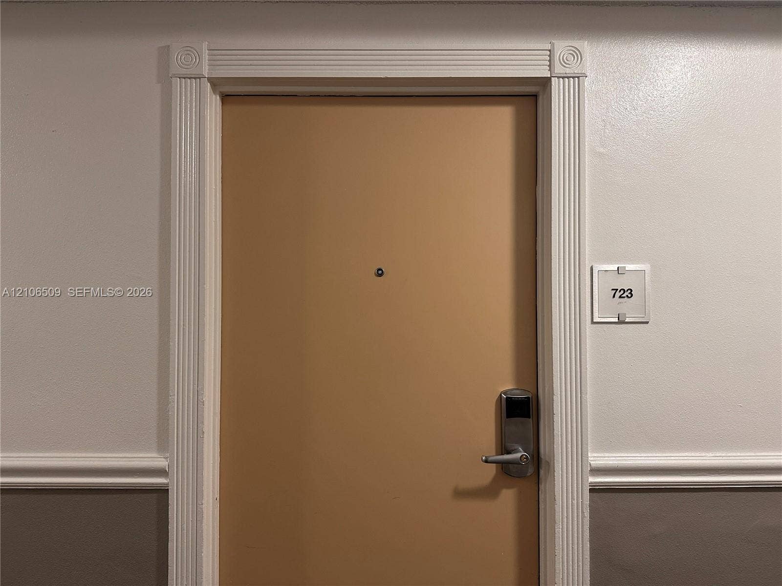 Entry door featuring fluted casing, decorative corner rosettes, a door viewer, and a digital handle lockset