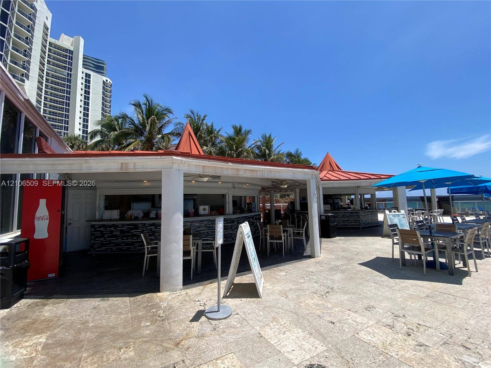 Outdoor covered bar area featuring red metal roofing, decorative stone facade, stone-paver flooring, and ceiling fans