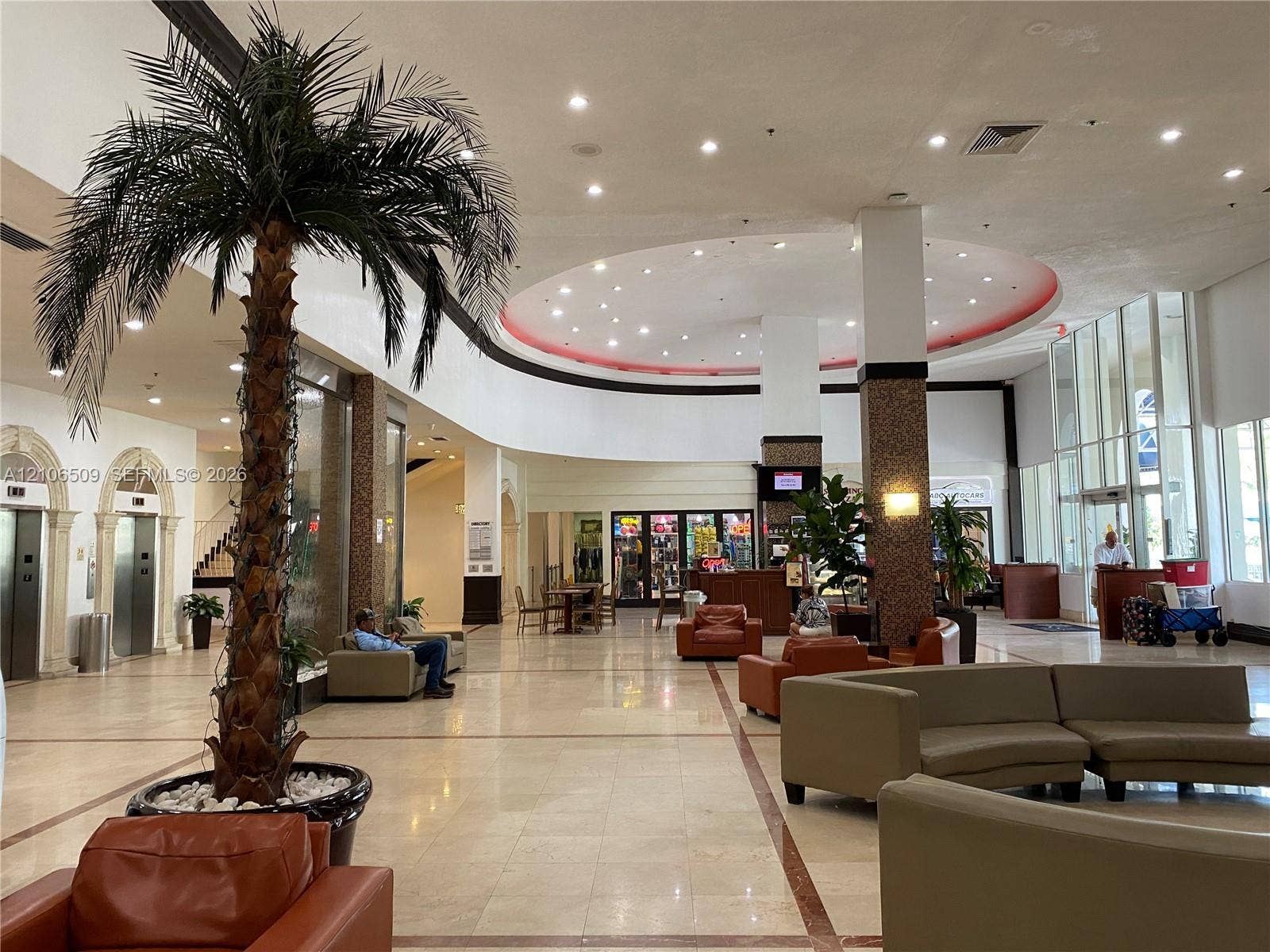 Expansive lobby featuring polished stone flooring, arched elevator entrances with stone detailing, a circular recessed ceiling with integrated lighting, and full-height floor-to-ceiling windows