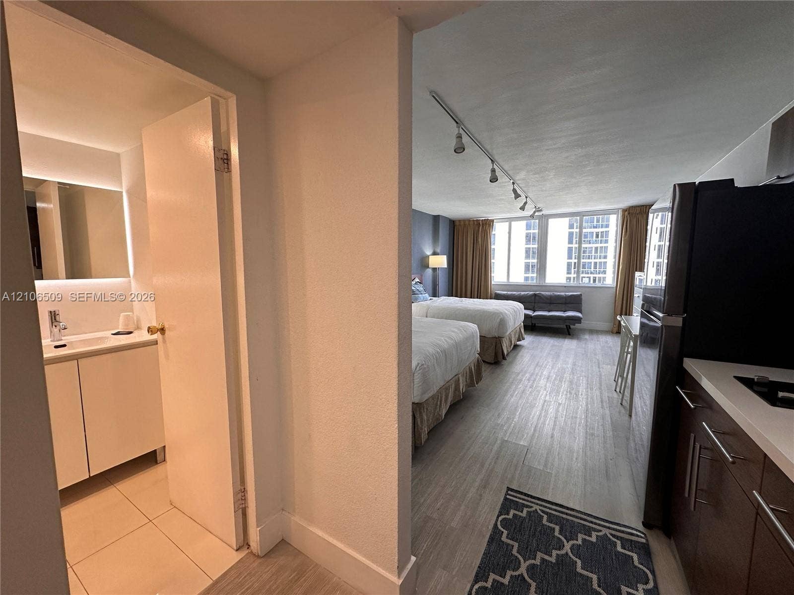 Bathroom featuring a vanity with integrated sink and backlit mirror, wood-finish flooring, track lighting, and a kitchenette equipped with cabinetry and stone-surfaced countertops