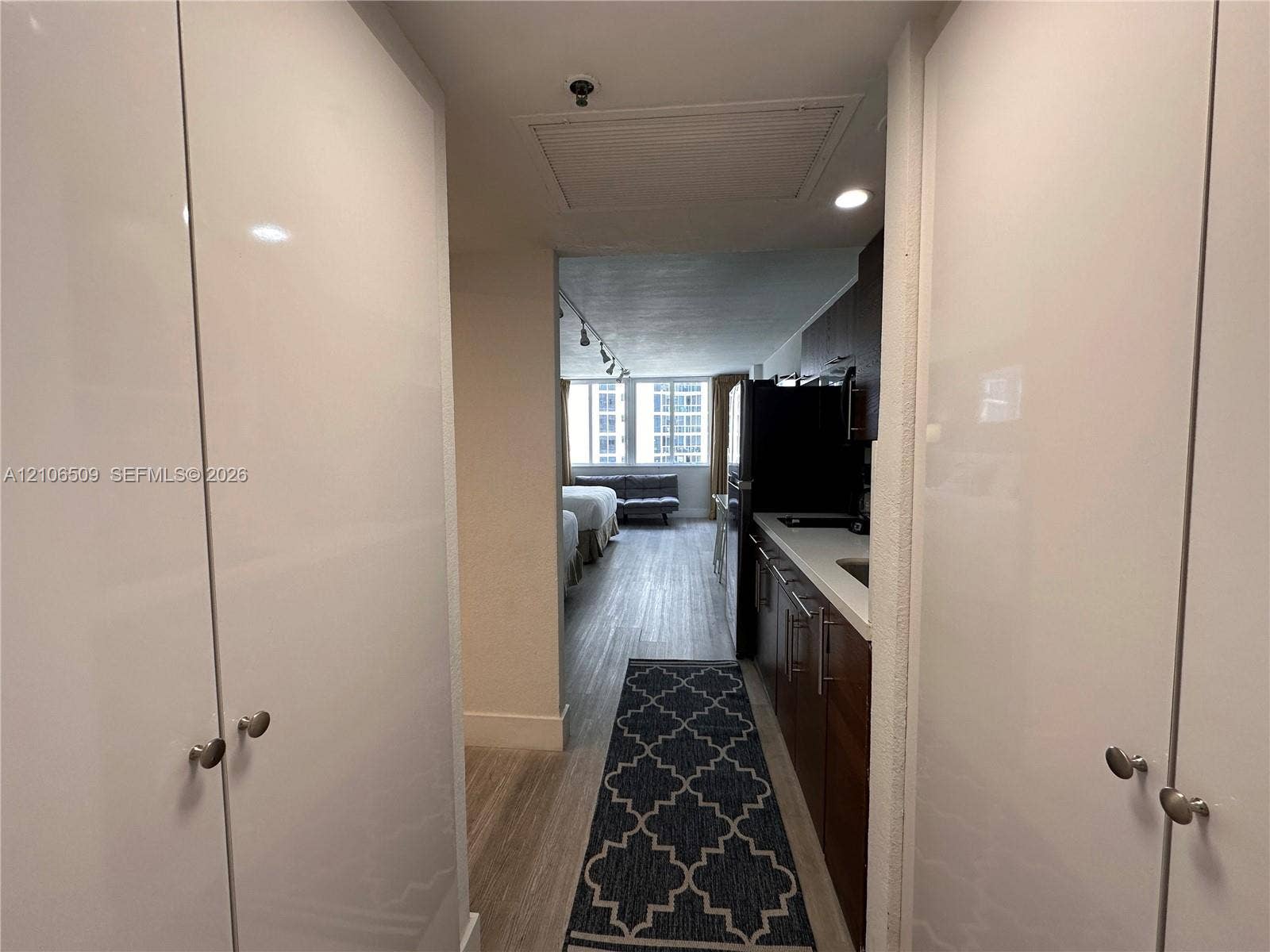 Entryway featuring dual floor-to-ceiling white cabinetry, wood-finish flooring, and galley-style kitchen with dark cabinetry and light-toned solid surface countertops