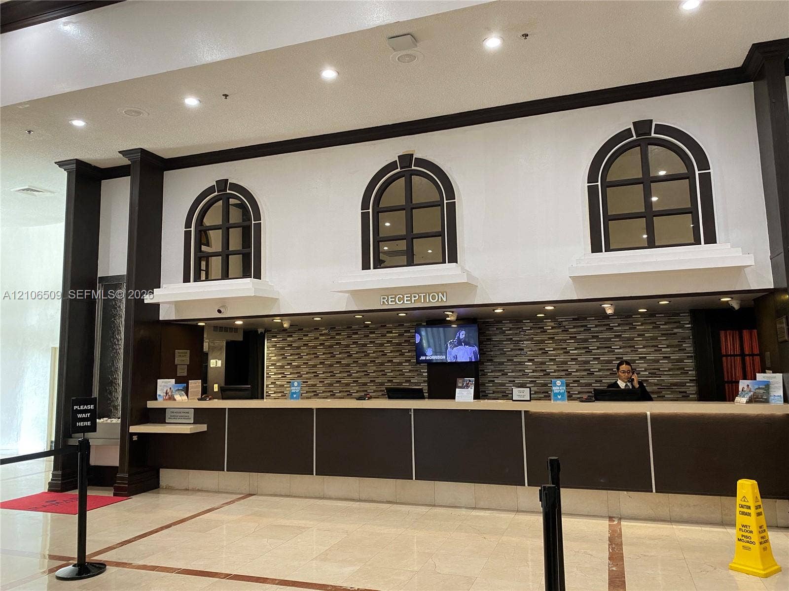 Reception area featuring a multi-tiered front desk, stone-tiled backsplash, recessed lighting, and arched decorative window accents with dark-finished trim