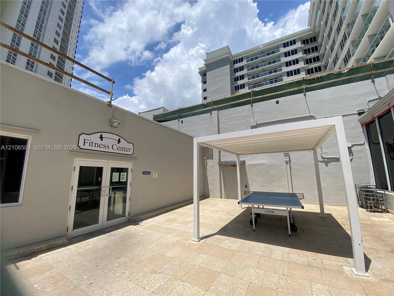 Outdoor patio featuring stone-tiled flooring, a white pergola structure, and access to a fitness center