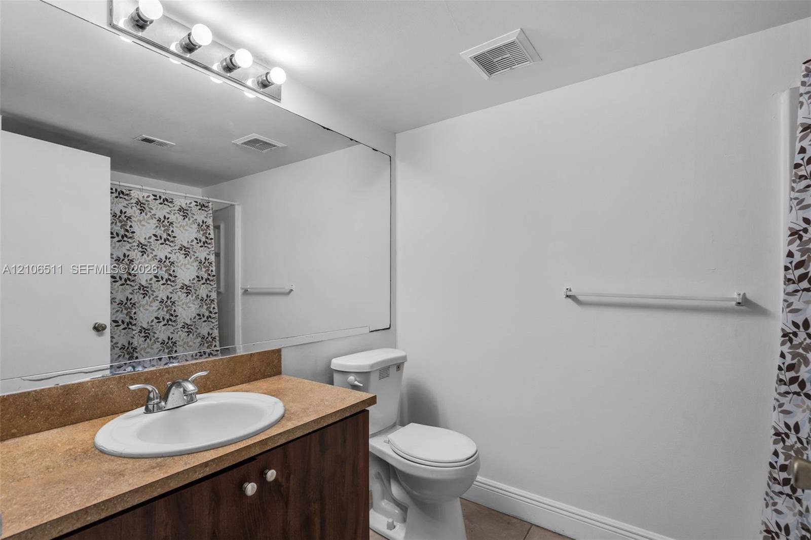 3229 Coral Lake Drive, #3229, Coral Springs, FL 33065 Bathroom featuring a wood-finish vanity with a solid-surface countertop, an integrated oval sink, a full-width wall mirror, and a multi-bulb light fixture