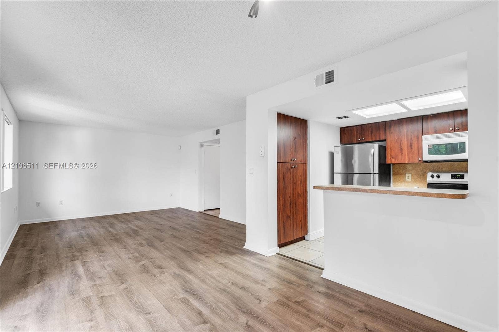 3229 Coral Lake Drive, #3229, Coral Springs, FL 33065 Open-concept interior featuring wood-finish flooring, kitchen cabinetry with a dark wood finish, stainless steel refrigerator, and recessed kitchen lighting