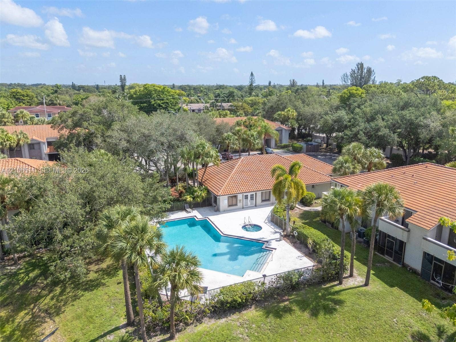 3229 Coral Lake Drive, #3229, Coral Springs, FL 33065 Community pool featuring an attached spa, expansive concrete pool deck, tile roofing, and mature palm trees