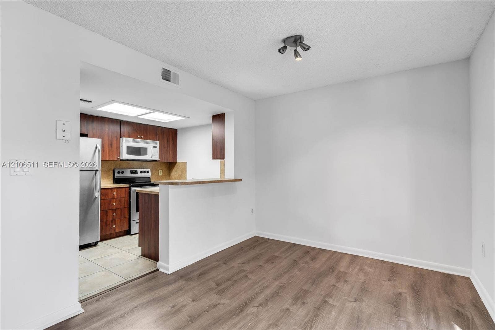 3229 Coral Lake Drive, #3229, Coral Springs, FL 33065 Kitchen featuring wood-finish cabinetry, stainless steel appliances, neutral tile flooring, wood-finish flooring, and a breakfast bar
