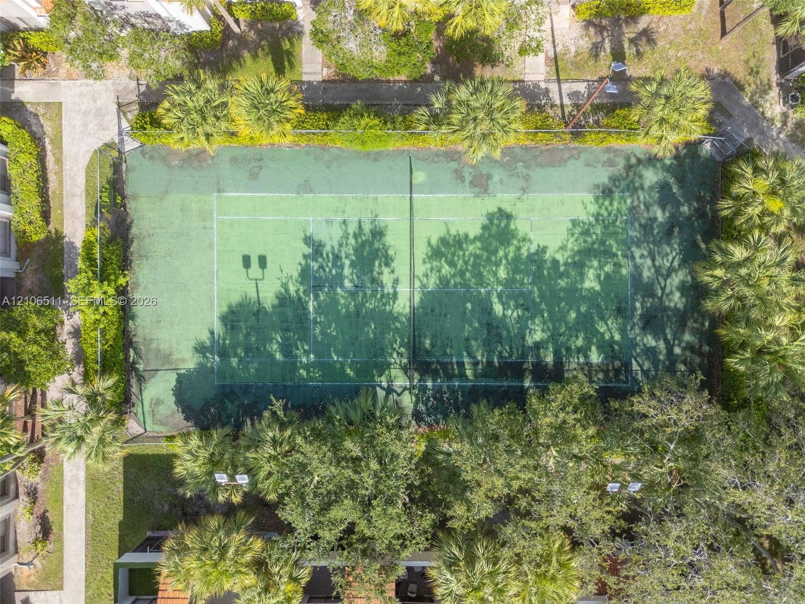 3229 Coral Lake Drive, #3229, Coral Springs, FL 33065 Hard-surface tennis court featuring perimeter chain-link fencing, dual mounted pole lights, and surrounding mature landscaping