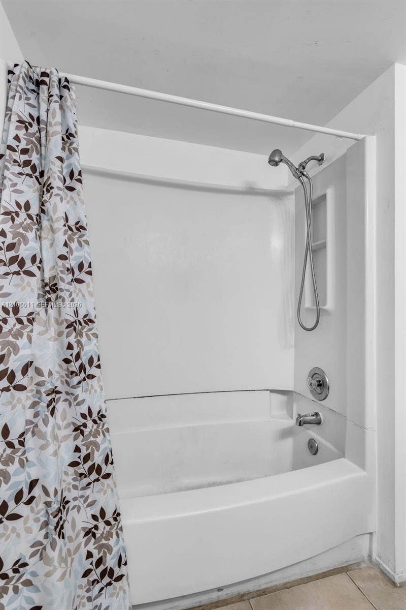 3229 Coral Lake Drive, #3229, Coral Springs, FL 33065 Bathtub and shower combination featuring a white surround, integrated shelving, handheld showerhead, and metal hardware