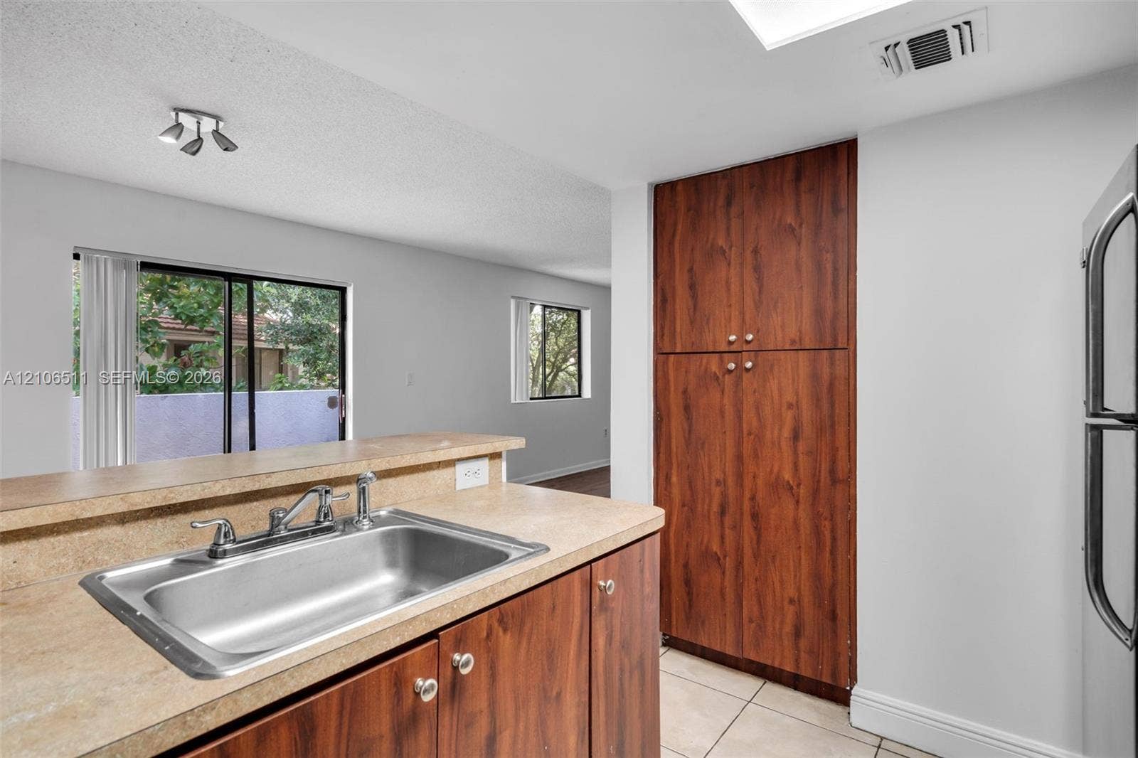 3229 Coral Lake Drive, #3229, Coral Springs, FL 33065 Kitchen featuring wood-finish cabinetry, neutral solid-surface countertops, a stainless steel dual-basin sink with a metallic faucet, and ceramic tile flooring