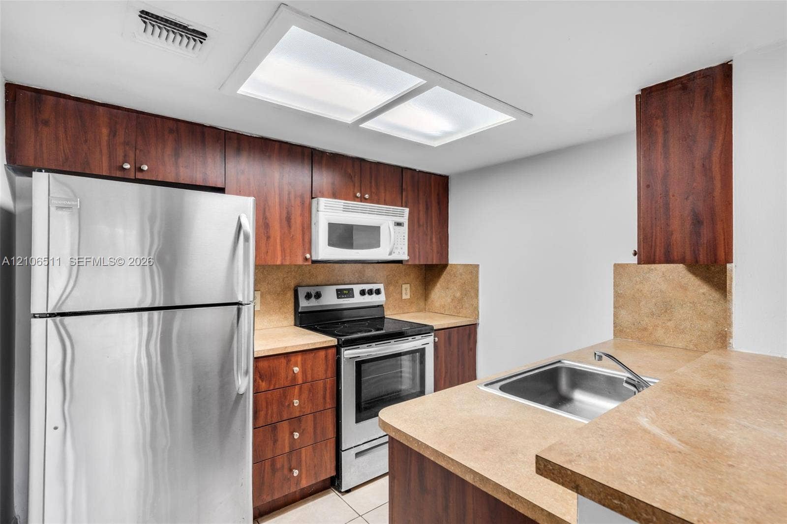 3229 Coral Lake Drive, #3229, Coral Springs, FL 33065 Kitchen featuring dark-toned wood cabinetry, stainless steel refrigerator and range, integrated microwave, and neutral-toned countertops with a stainless steel sink