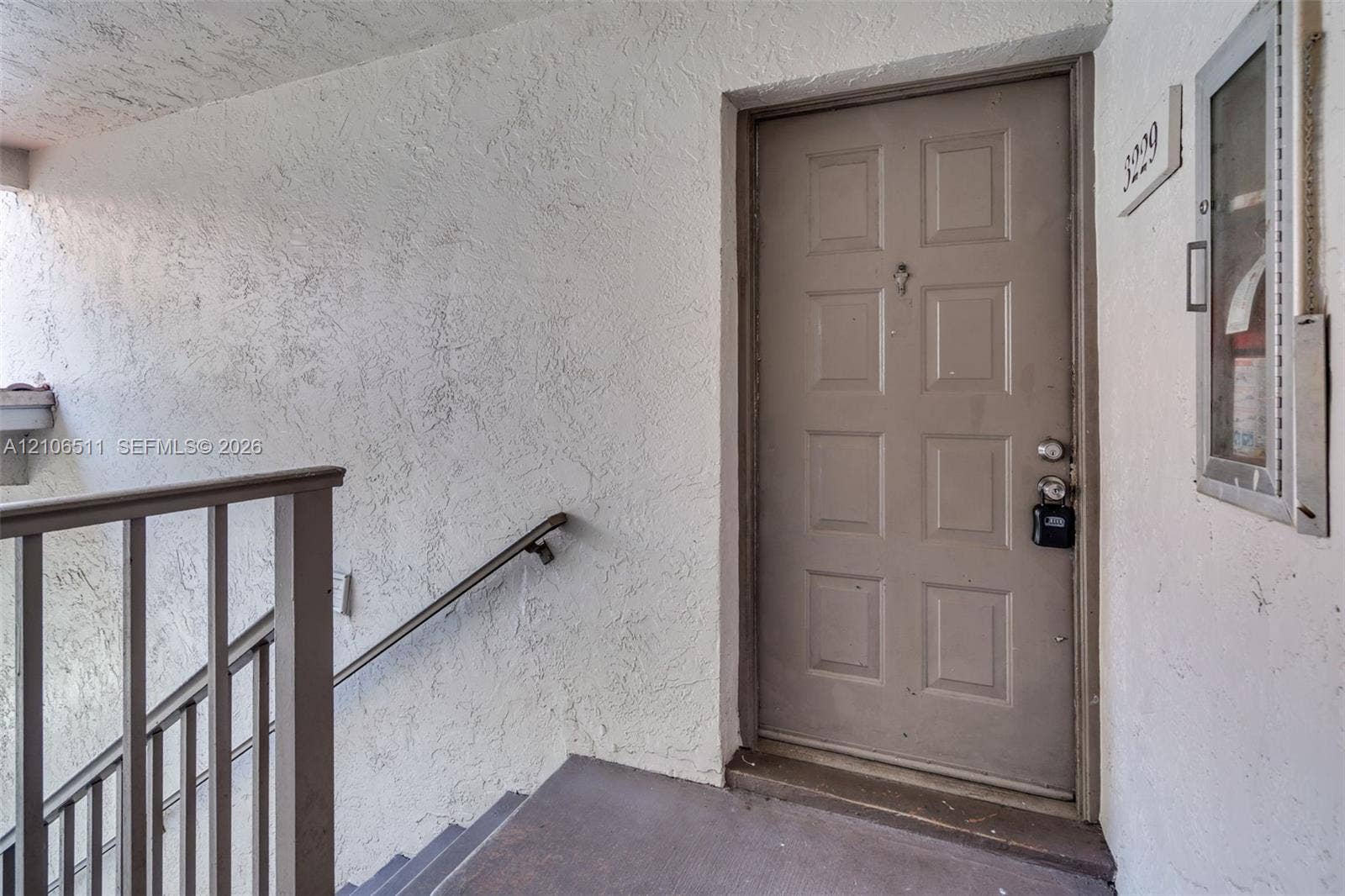 3229 Coral Lake Drive, #3229, Coral Springs, FL 33065 Exterior entryway featuring a solid-core eight-panel door, textured stucco wall finish, and metal stair railing