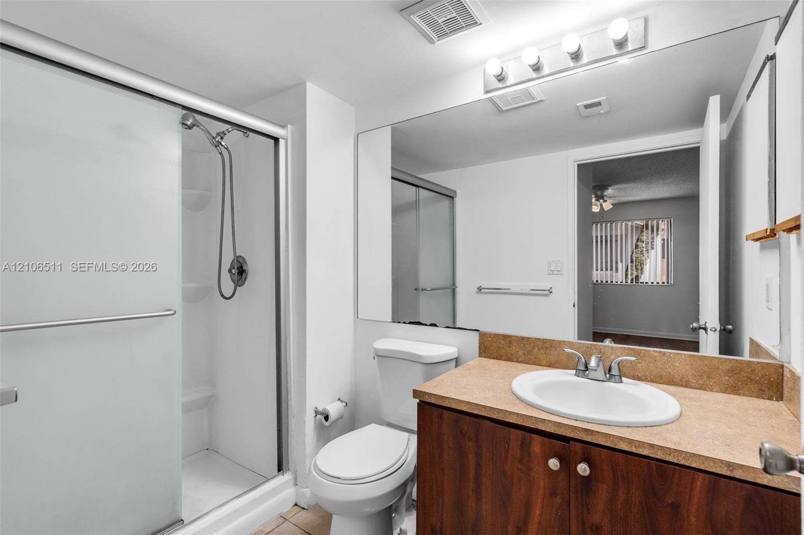 3229 Coral Lake Drive, #3229, Coral Springs, FL 33065 Bathroom featuring a shower stall with a sliding glass door, wood-finish vanity cabinet, solid-surface countertop with an integrated basin, and full-width wall mirror