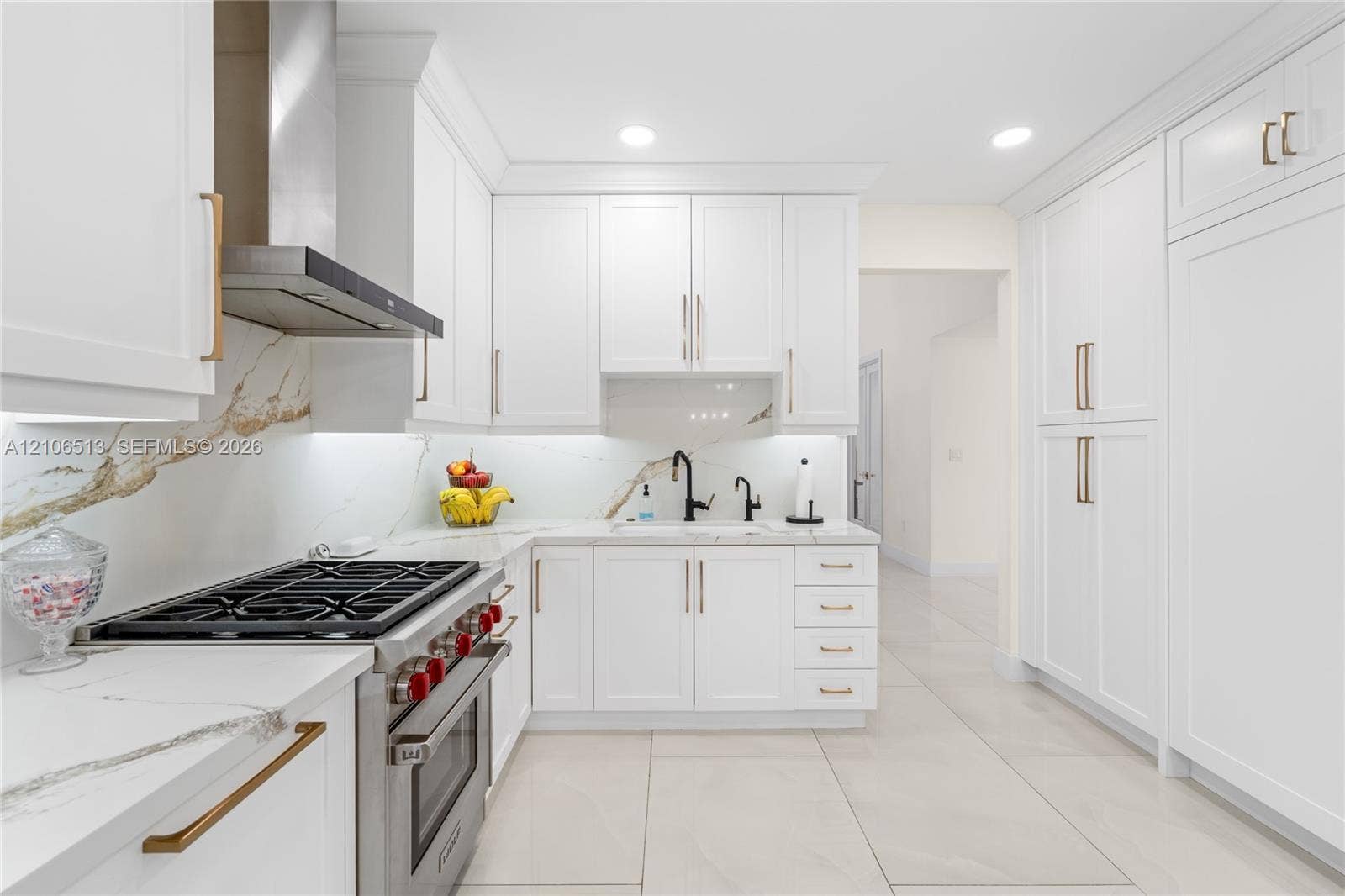5720 SW 128th Street, Pinecrest, FL 33156 Kitchen featuring shaker-style white cabinetry, stone-finish countertops with matching full-height backsplash, stainless steel gas range with overhead vent hood, under-cabinet lighting, and large-format tile flooring