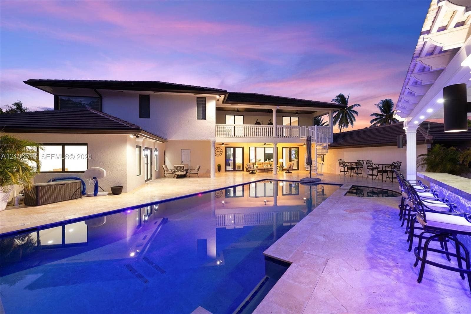 5720 SW 128th Street, Pinecrest, FL 33156 Rear exterior featuring a custom swimming pool with integrated spa, stone-paver decking, built-in swim-up bar, and second-level balcony with white railings