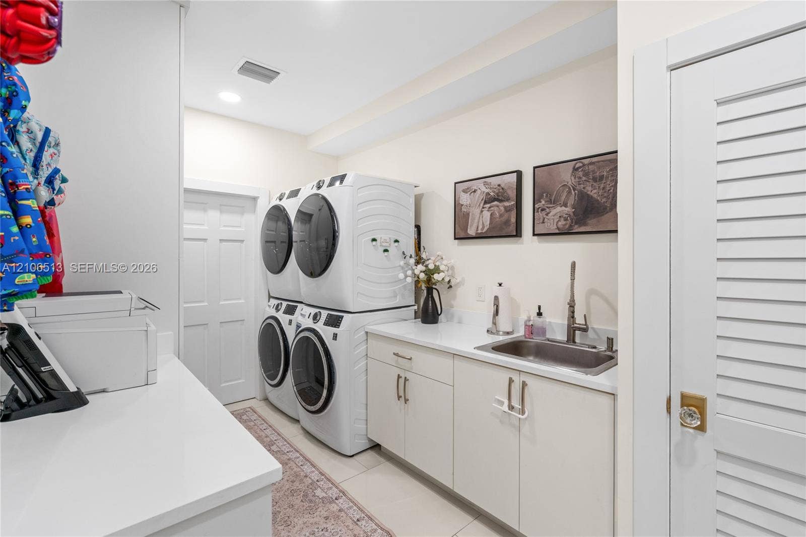5720 SW 128th Street, Pinecrest, FL 33156 Laundry room featuring stacked washer and dryer units, solid-surface countertops, an undermount stainless steel sink with a high-arch faucet, custom flat-panel cabinetry, and louvered door access