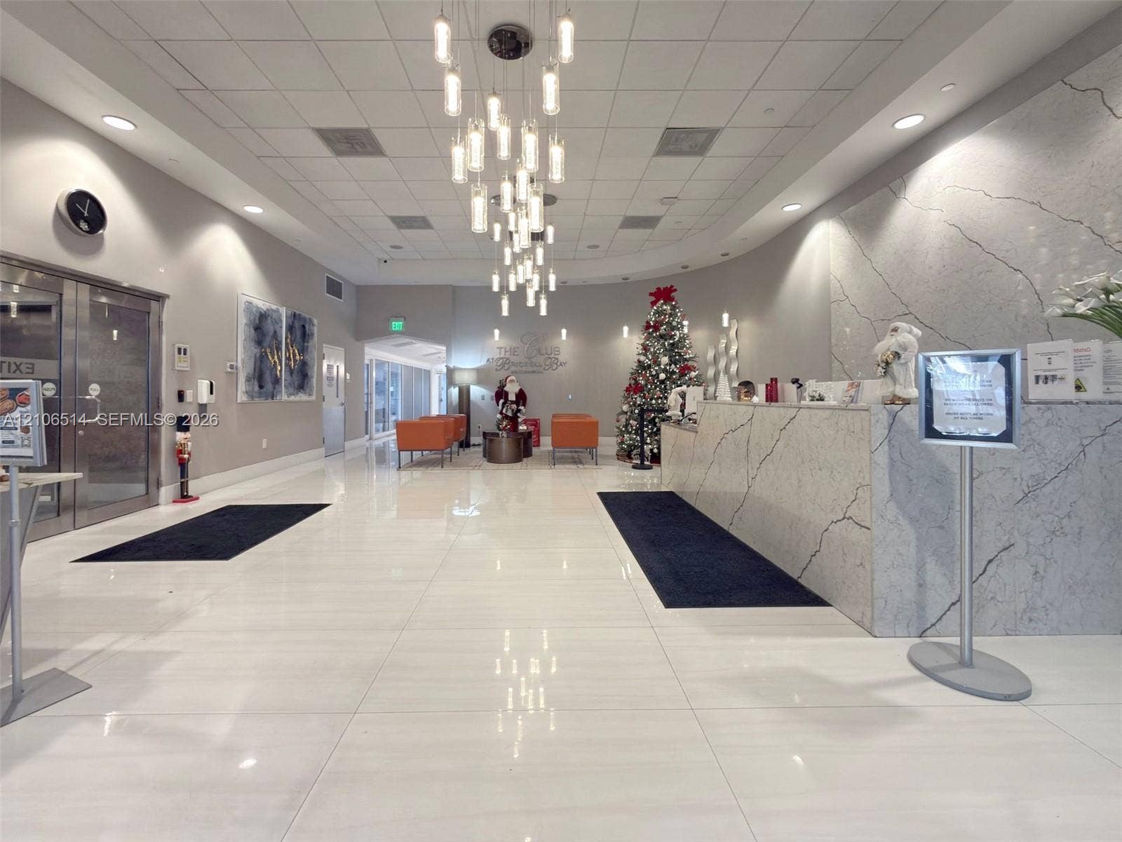 Grand lobby featuring polished tile flooring, a multi-tiered glass pendant chandelier, and a reception desk finished in stone surfacing with veining detail