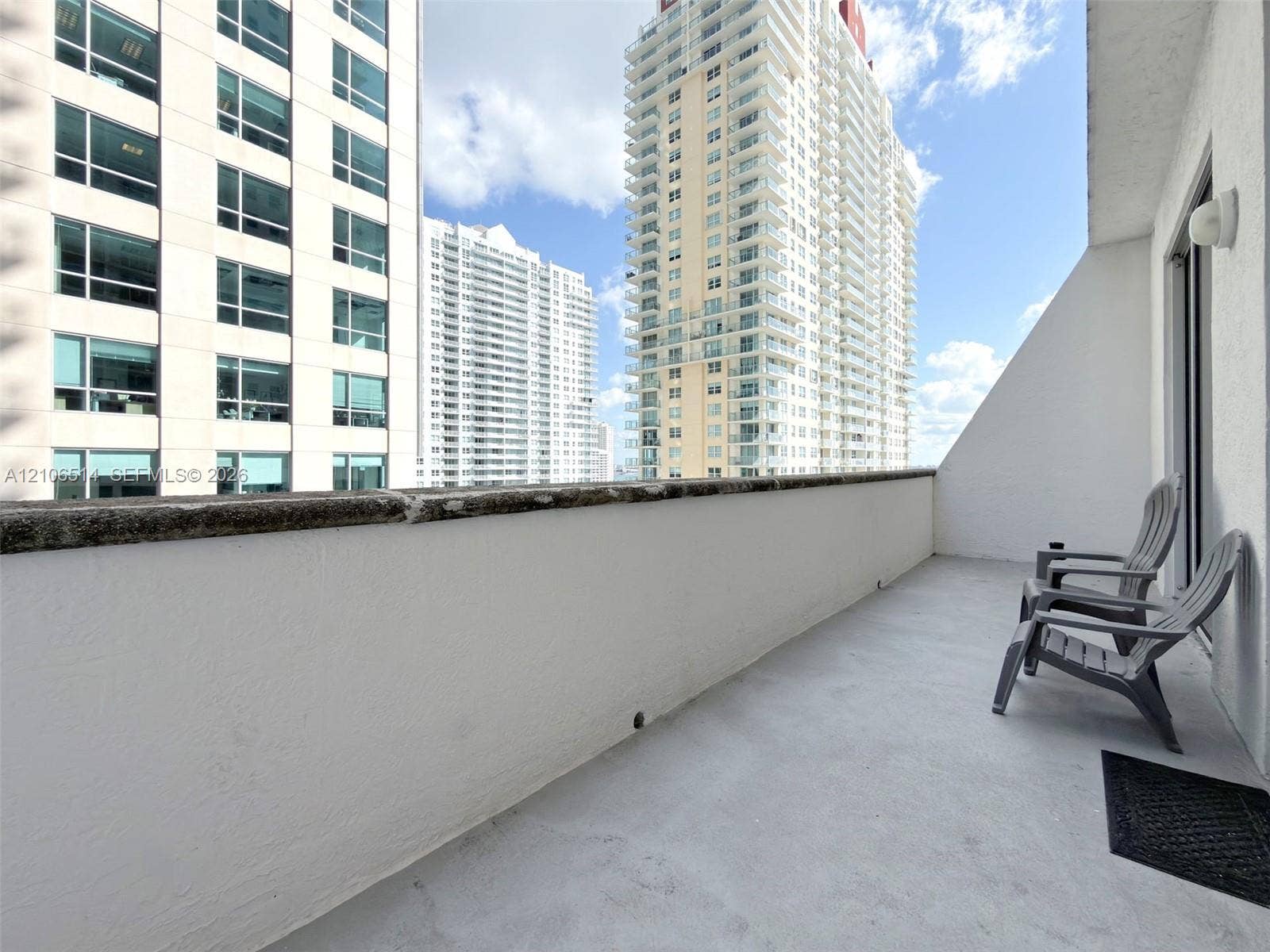 Covered balcony with smooth concrete flooring, solid masonry railing, and exterior wall-mounted lighting