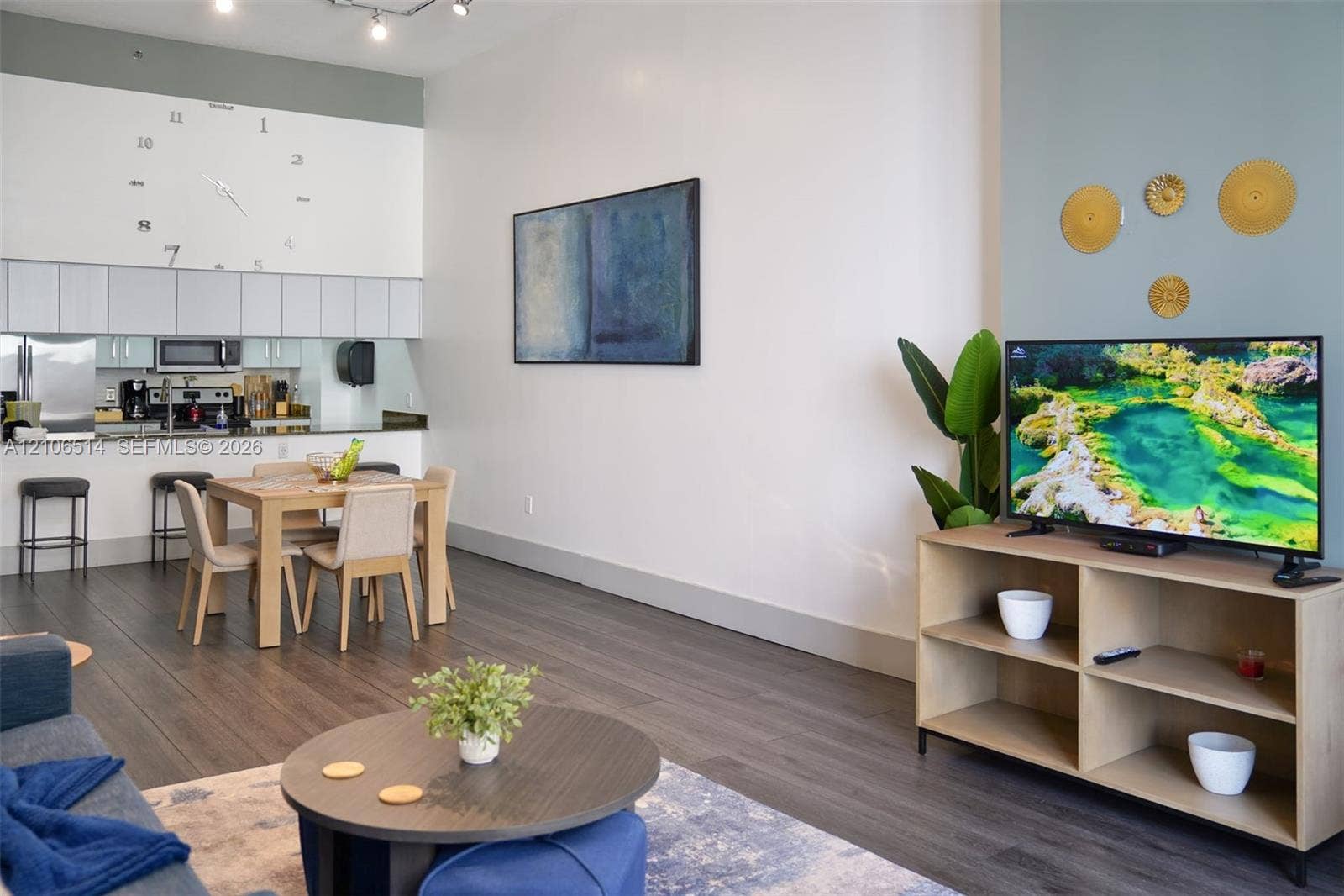 High-ceiling living area featuring dark wood-finish flooring, white upper cabinetry, a stone-surface breakfast bar, and track lighting