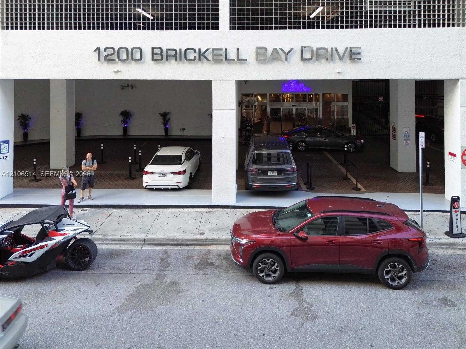 Covered entrance featuring valet drop-off area, high-visibility building signage, and structural concrete pillars