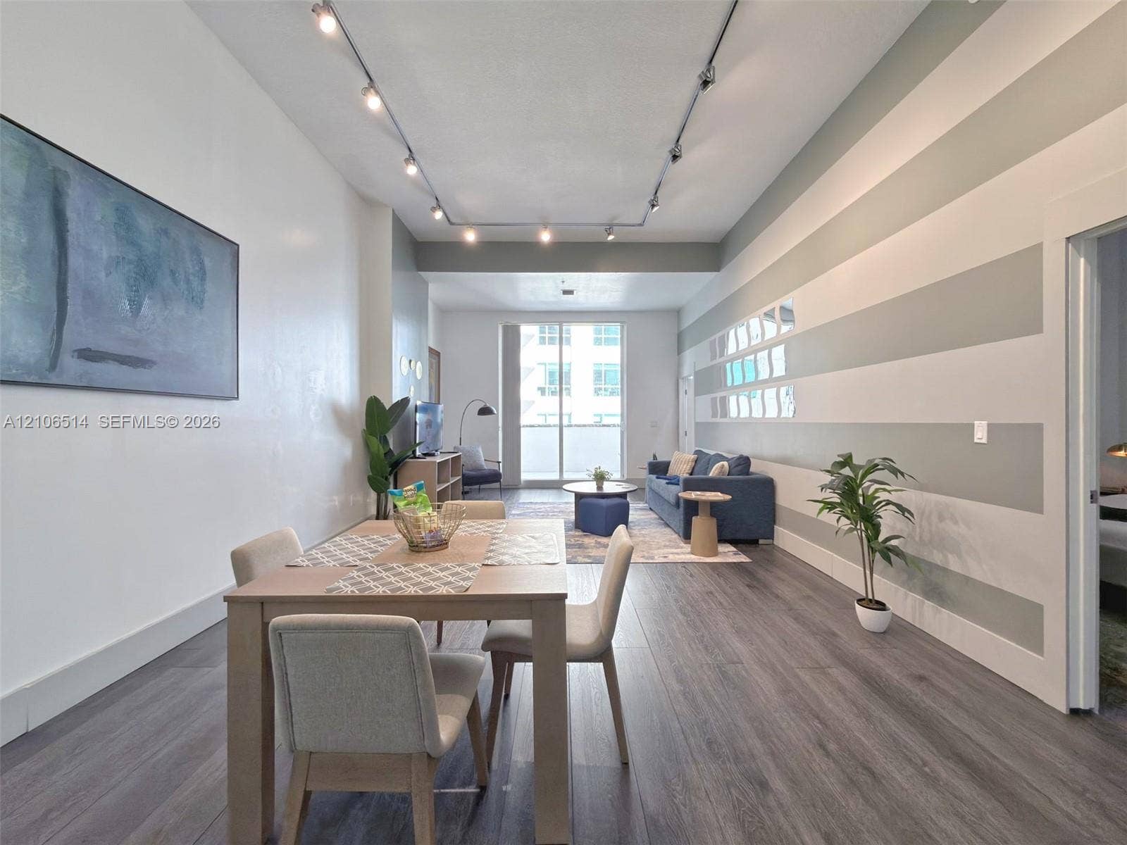 Open-concept interior featuring wood-finish flooring, high ceilings, ceiling-mounted track lighting, and a sliding glass door
