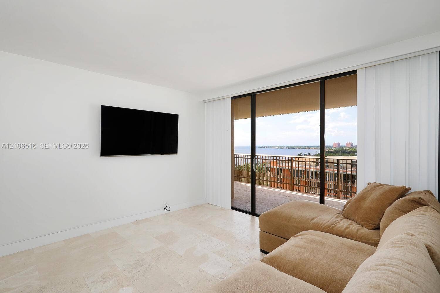 Large-format light stone flooring, floor-to-ceiling sliding glass doors, and a covered exterior balcony featuring a metal railing