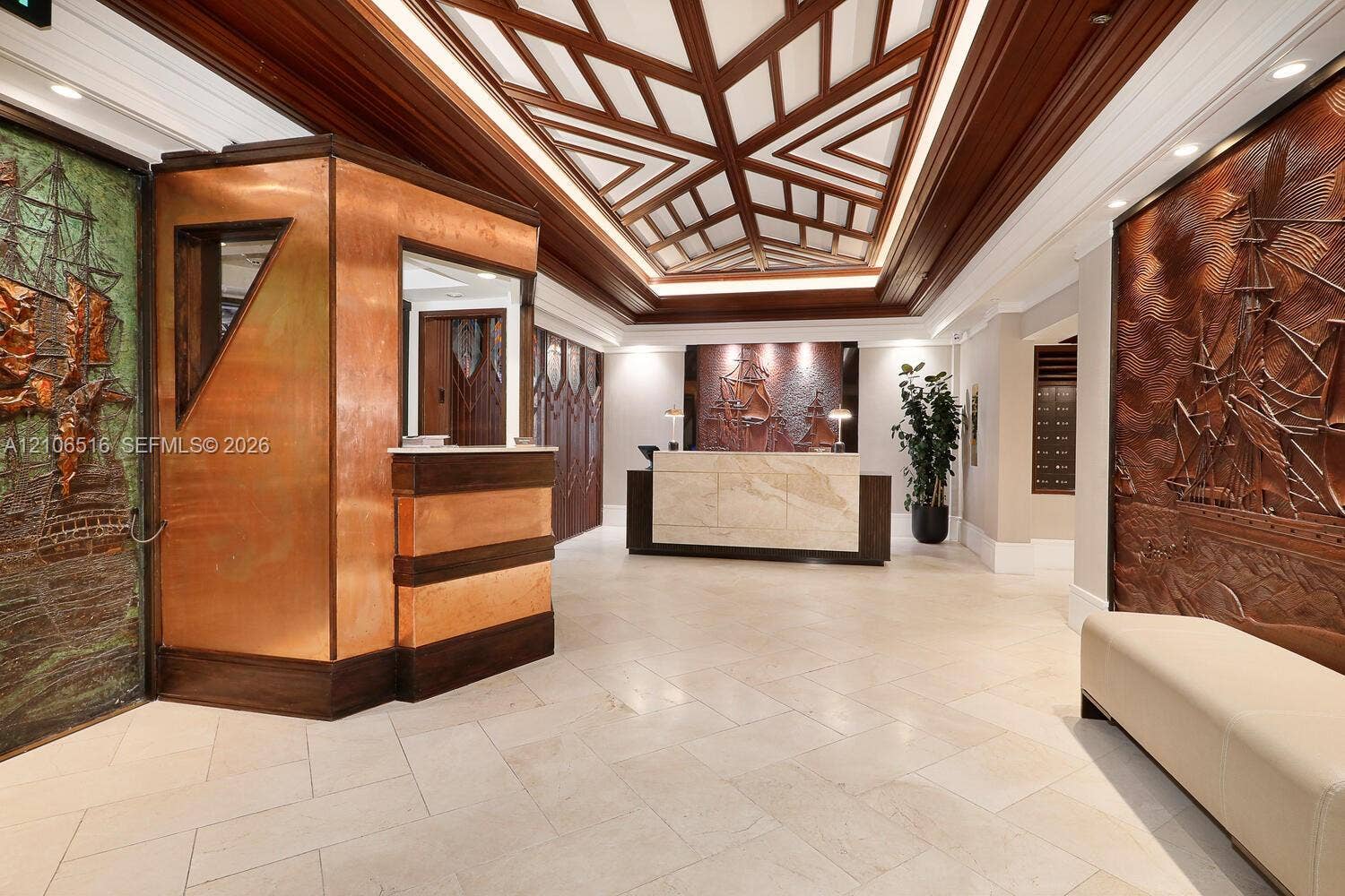 Lobby featuring a geometric coffered wood ceiling, polished stone flooring, custom copper wall cladding, and relief-carved ship murals