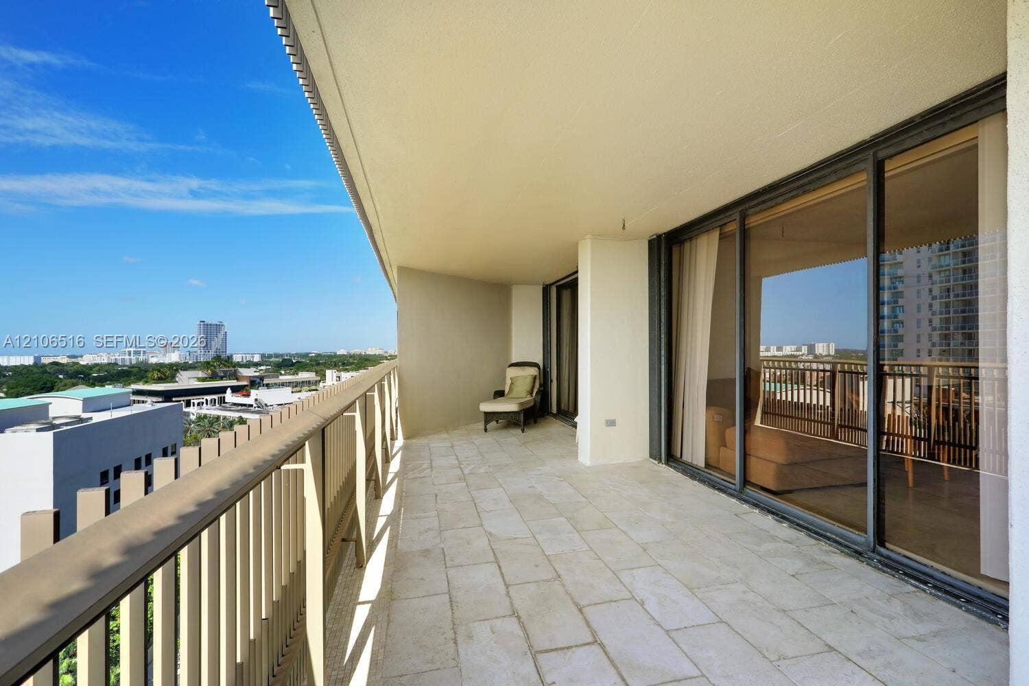 Expansive covered balcony featuring stone tile flooring, vertical slat metal railing, and floor-to-ceiling glass sliding doors