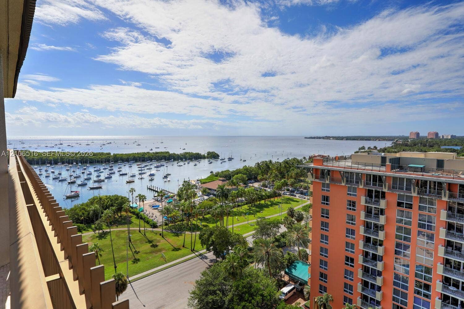 Elevated balcony with vertical railing, overlooking coastal waters, boat mooring, and landscaped grounds