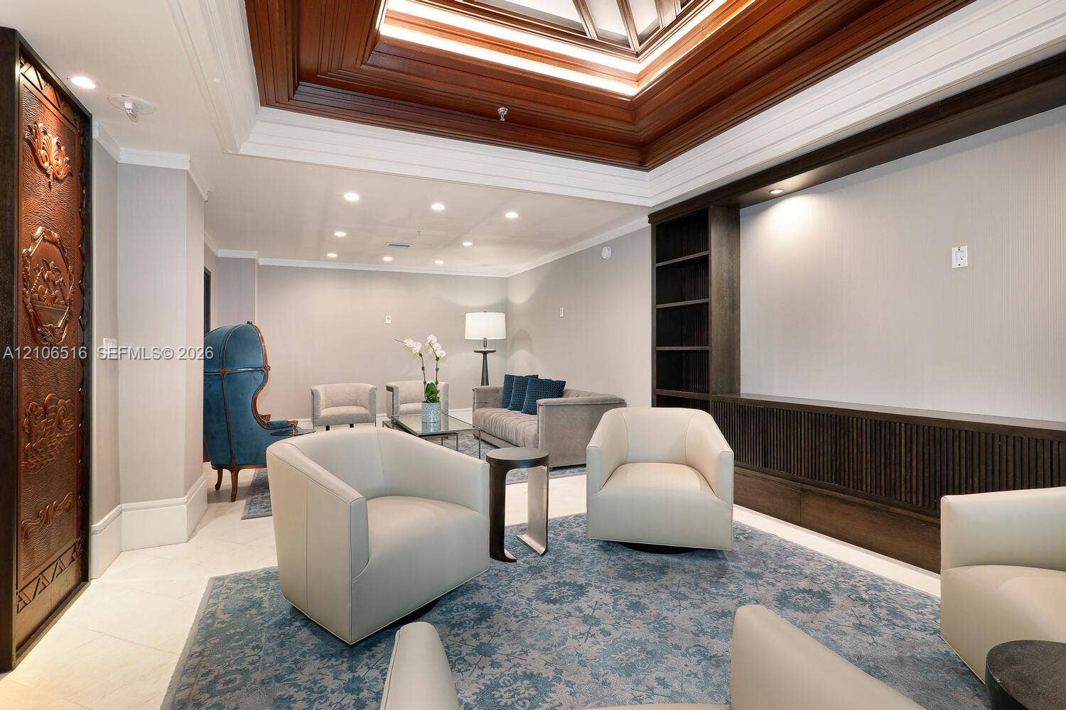 Coffered ceiling with integrated crown molding, custom dark wood-finish built-in shelving, decorative metallic door panel, recessed lighting, and tile flooring