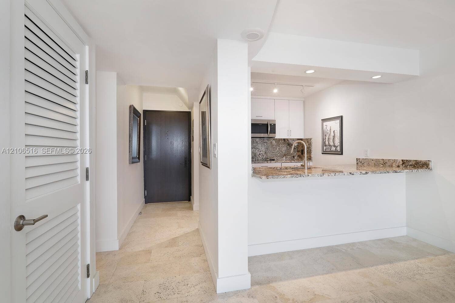 Natural stone flooring, kitchen pass-through counter, louvered closet door, track lighting, and solid-core interior door