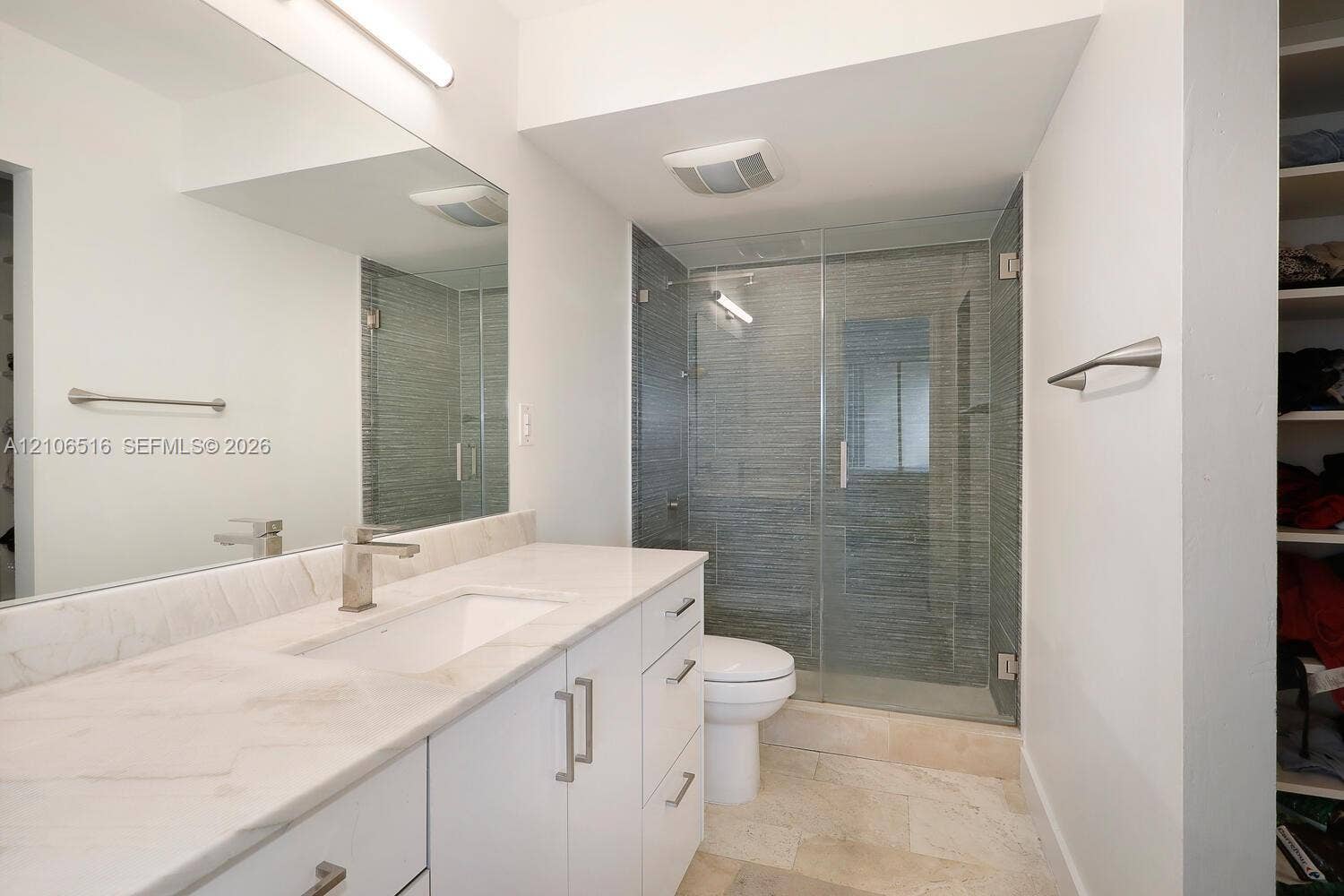 Bathroom featuring a white vanity with a stone countertop, an integrated rectangular sink, a full-width wall mirror, and a glass-enclosed shower with textured tile surround