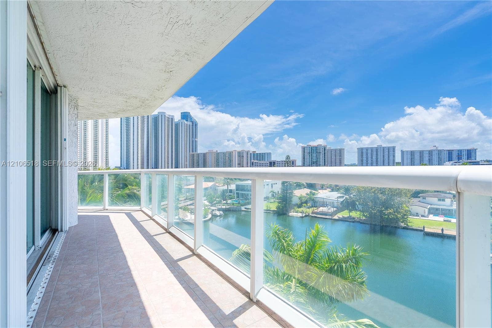 16500 Collins Avenue, #554, Sunny Isles Beach, FL 33160 Covered balcony featuring tile flooring and a glass-paneled railing overlooking the waterway and cityscape