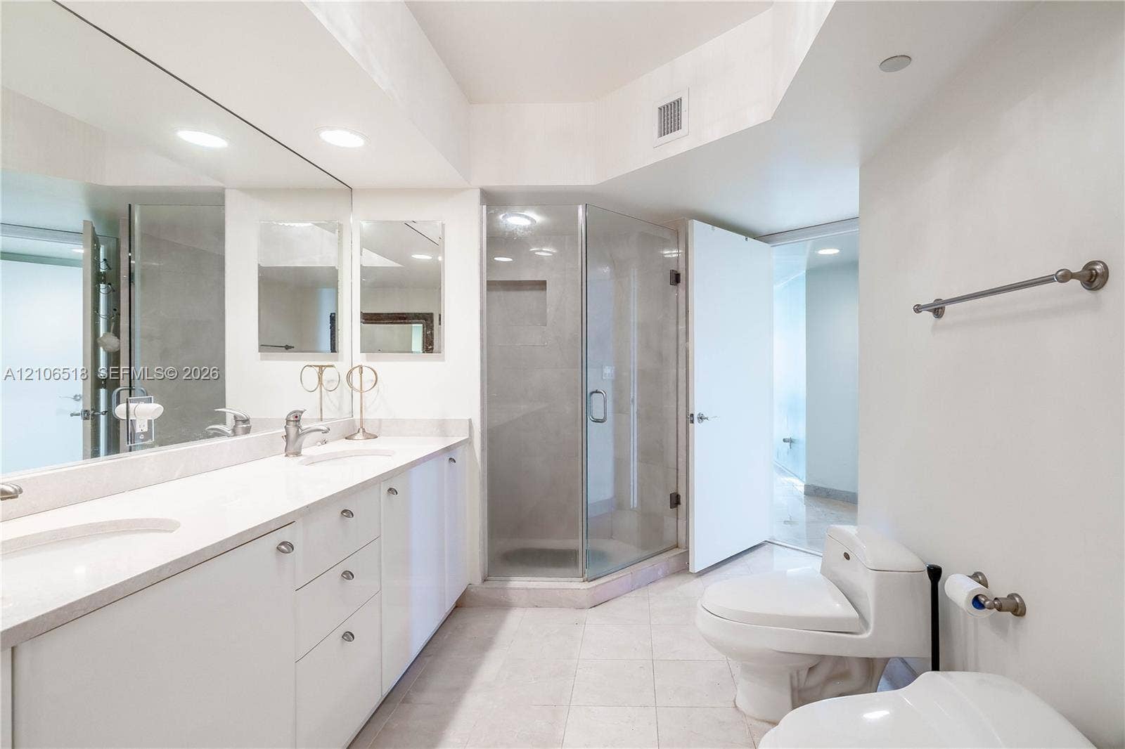 16500 Collins Avenue, #554, Sunny Isles Beach, FL 33160 Double vanity with white cabinetry and solid-surface countertop, full-width wall mirror, glass-enclosed corner shower with tiled interior, and ceramic tile flooring
