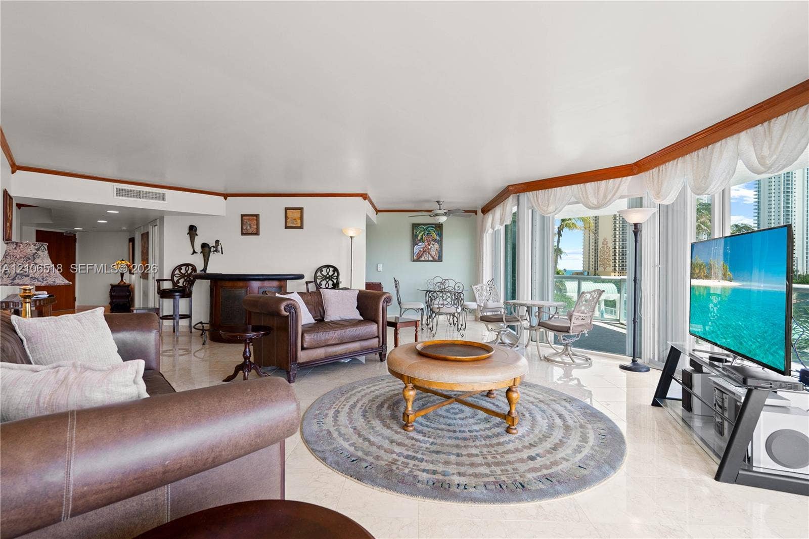 16500 Collins Avenue, #554, Sunny Isles Beach, FL 33160 Open-concept living area featuring polished stone flooring, custom wood crown molding, a built-in wet bar, and expansive glass sliding doors leading to a balcony