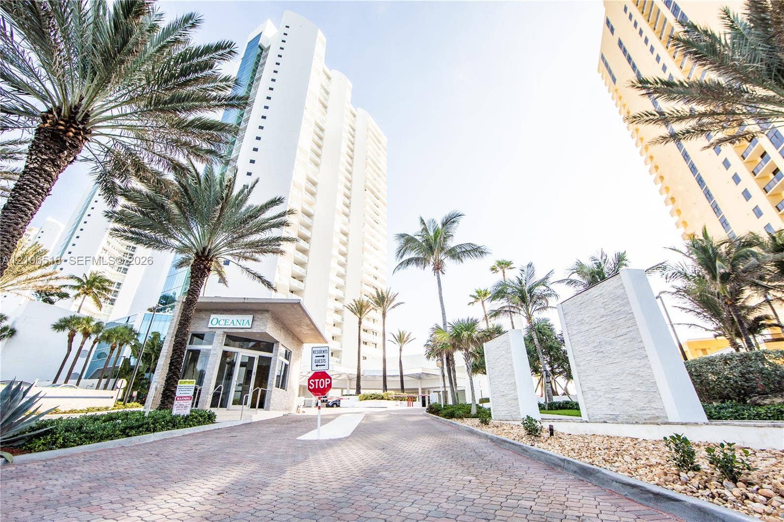 16500 Collins Avenue, #554, Sunny Isles Beach, FL 33160 High-rise exterior featuring a paved arrival courtyard, stacked-stone entrance pillars, and extensive mature palm tree landscaping