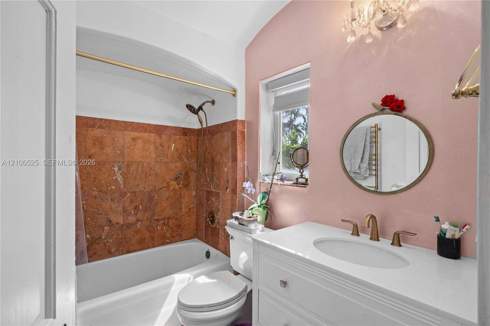 4760 N Bay Road, Miami Beach, FL 33140 Bathroom featuring a white vanity with an integrated basin, stone tile tub surround, gold-tone hardware, and a crystal chandelier