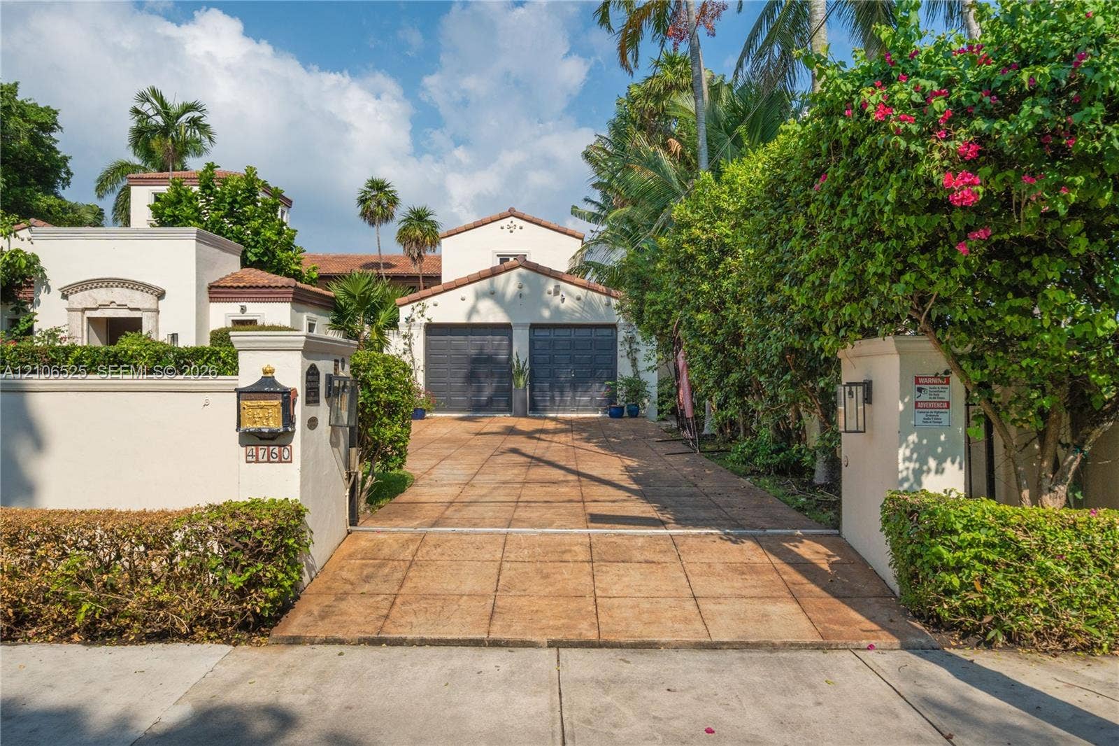 4760 N Bay Road, Miami Beach, FL 33140 Mediterranean-style stucco exterior featuring a gated entrance, terracotta-tiled roof, paver driveway, and a two-car garage