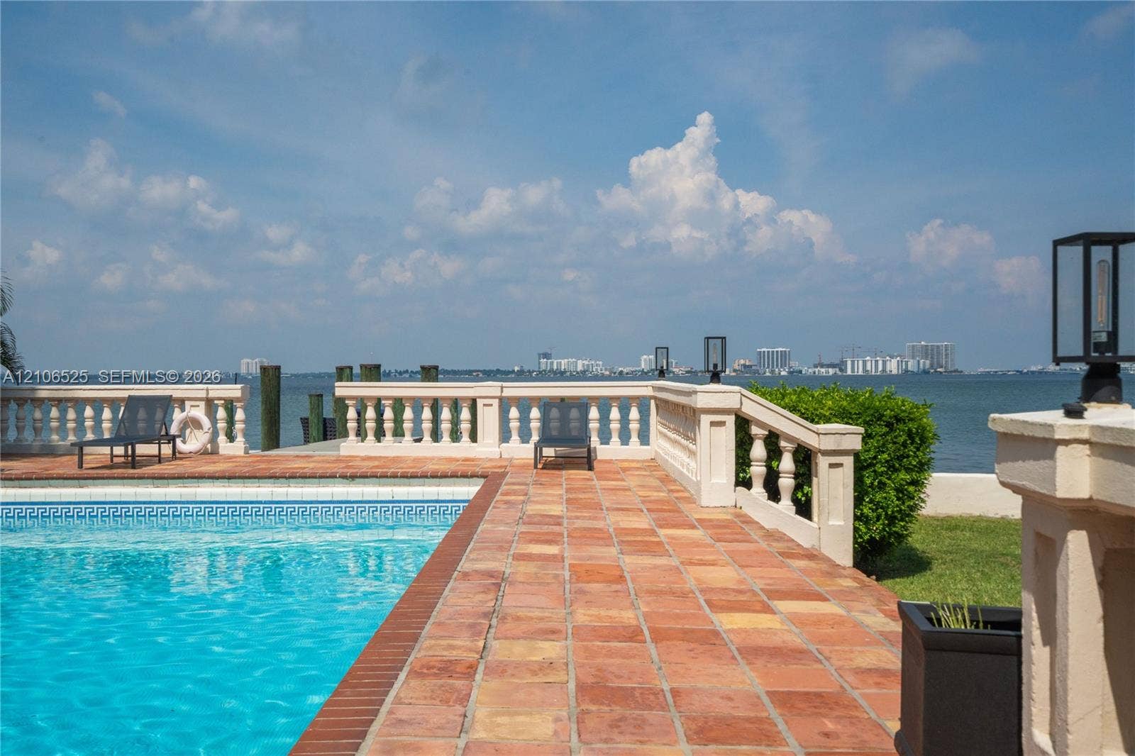 4760 N Bay Road, Miami Beach, FL 33140 In-ground swimming pool with tile border, terracotta tile patio, and concrete balustrade railing overlooking the water