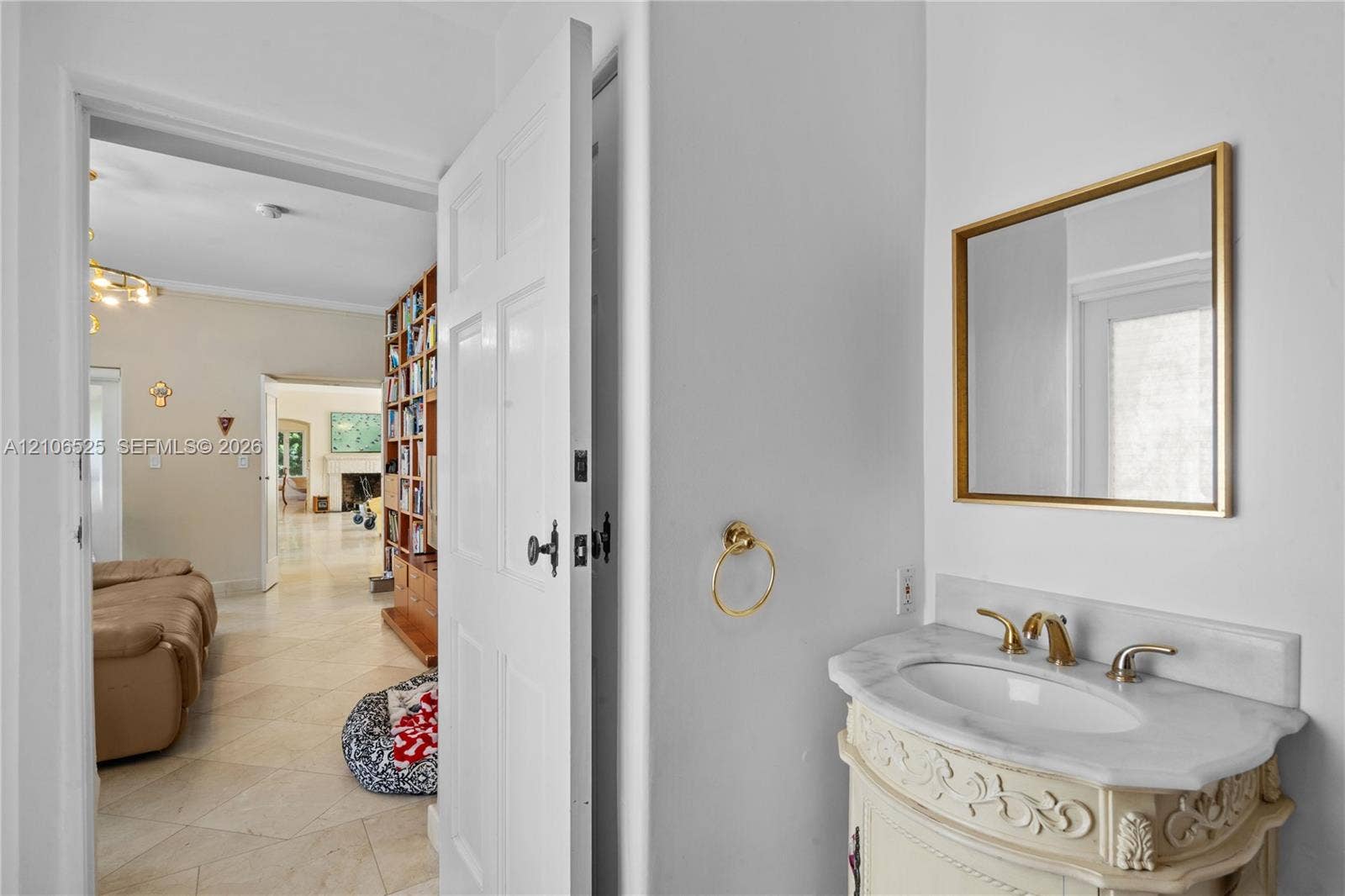4760 N Bay Road, Miami Beach, FL 33140 Custom vanity with an integrated stone countertop, oval undermount sink, brass finish widespread faucet, and matching brass-rimmed wall mirror