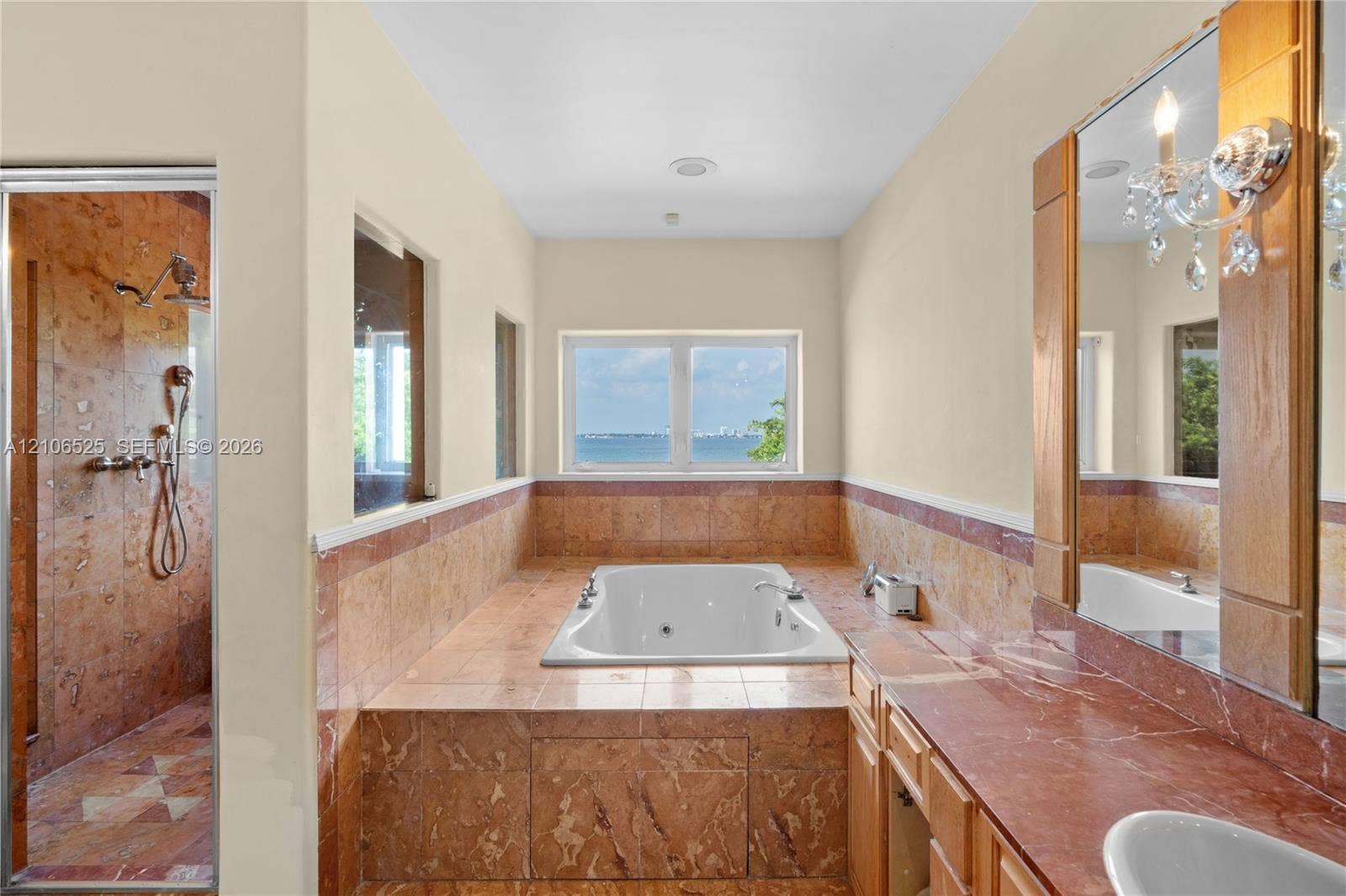 4760 N Bay Road, Miami Beach, FL 33140 Bathroom featuring a built-in soaking tub, natural stone tile surround, walk-in shower with stone tile walls, stone-topped vanity, and wall-mounted light fixtures