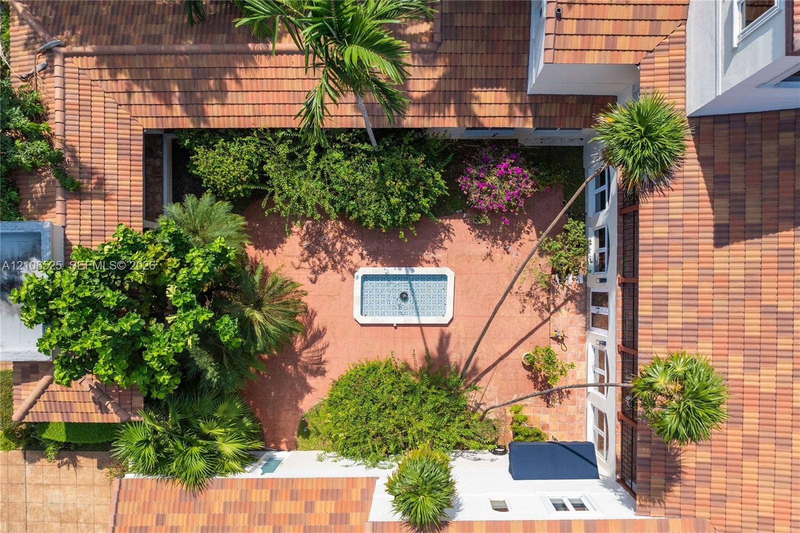 4760 N Bay Road, Miami Beach, FL 33140 Enclosed courtyard featuring a tiled roof, central rectangular fountain, landscaped greenery, and terracotta-style paving
