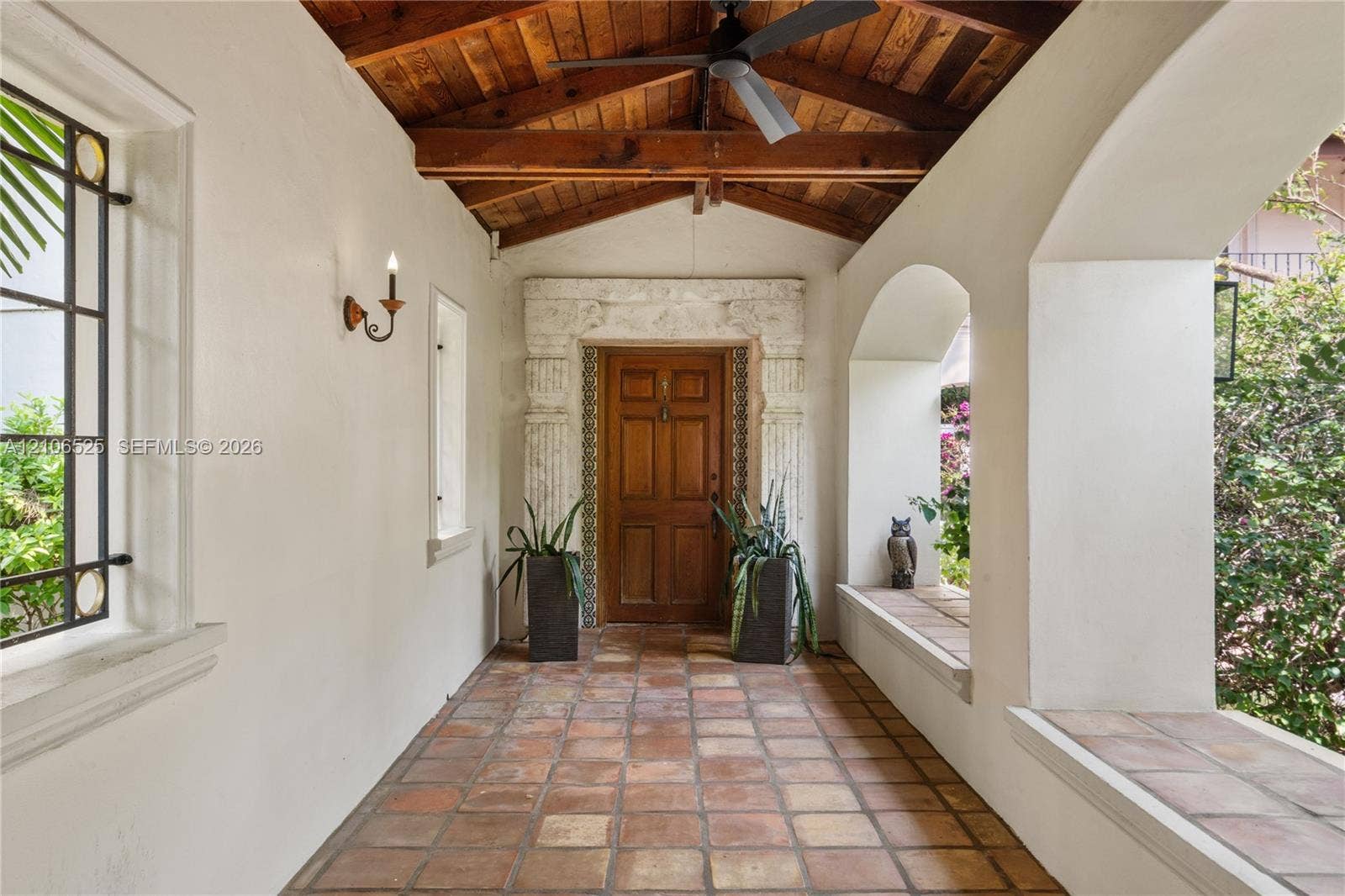 4760 N Bay Road, Miami Beach, FL 33140 Covered entryway featuring terracotta tile flooring, exposed wood-beam vaulted ceiling, arched masonry openings, stone door surround with column detailing, and built-in masonry seating