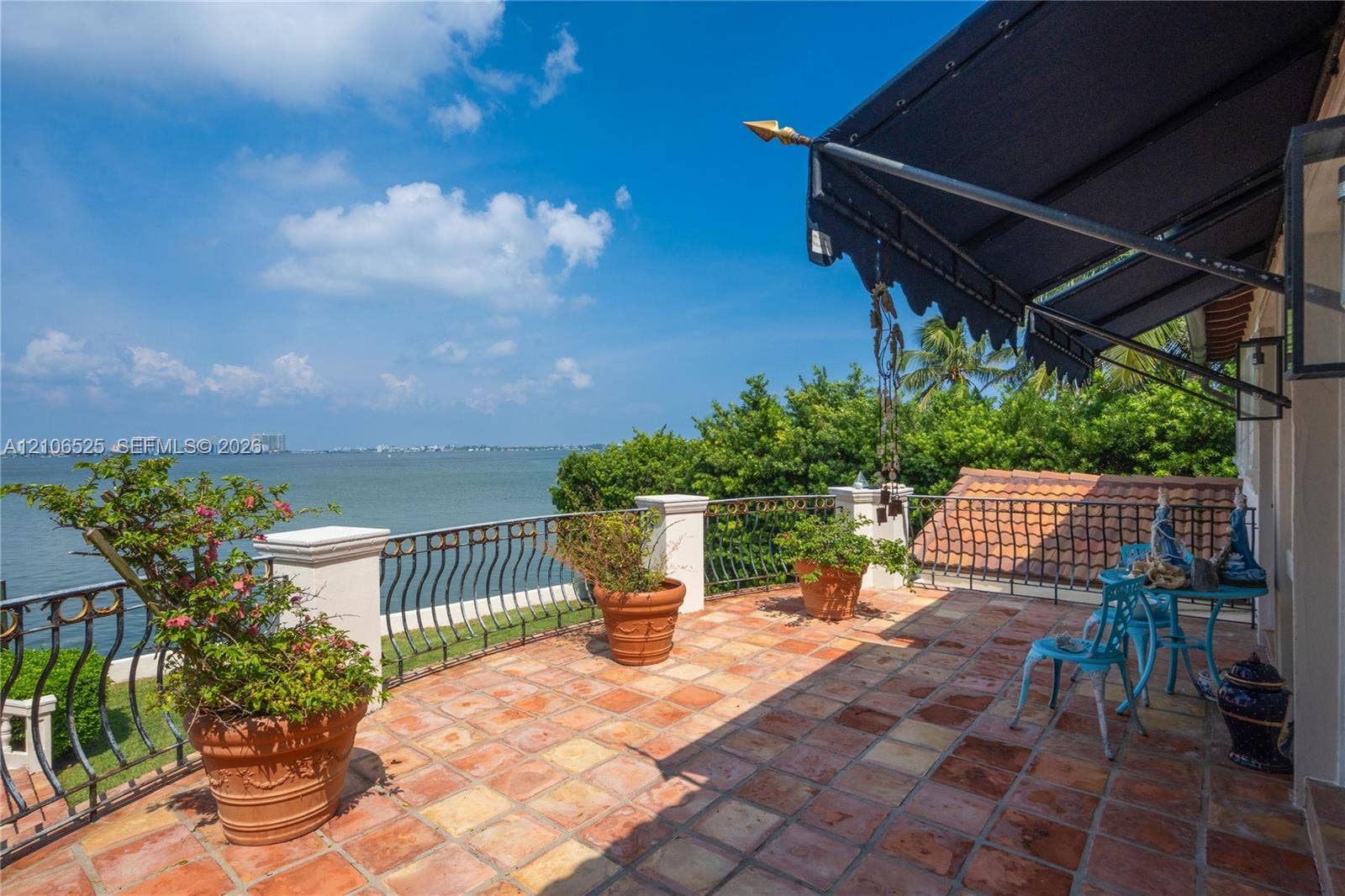 4760 N Bay Road, Miami Beach, FL 33140 Open-air terrace featuring terra-cotta tile flooring, ornate metal railing, retractable fabric awning, and unobstructed waterfront scenery