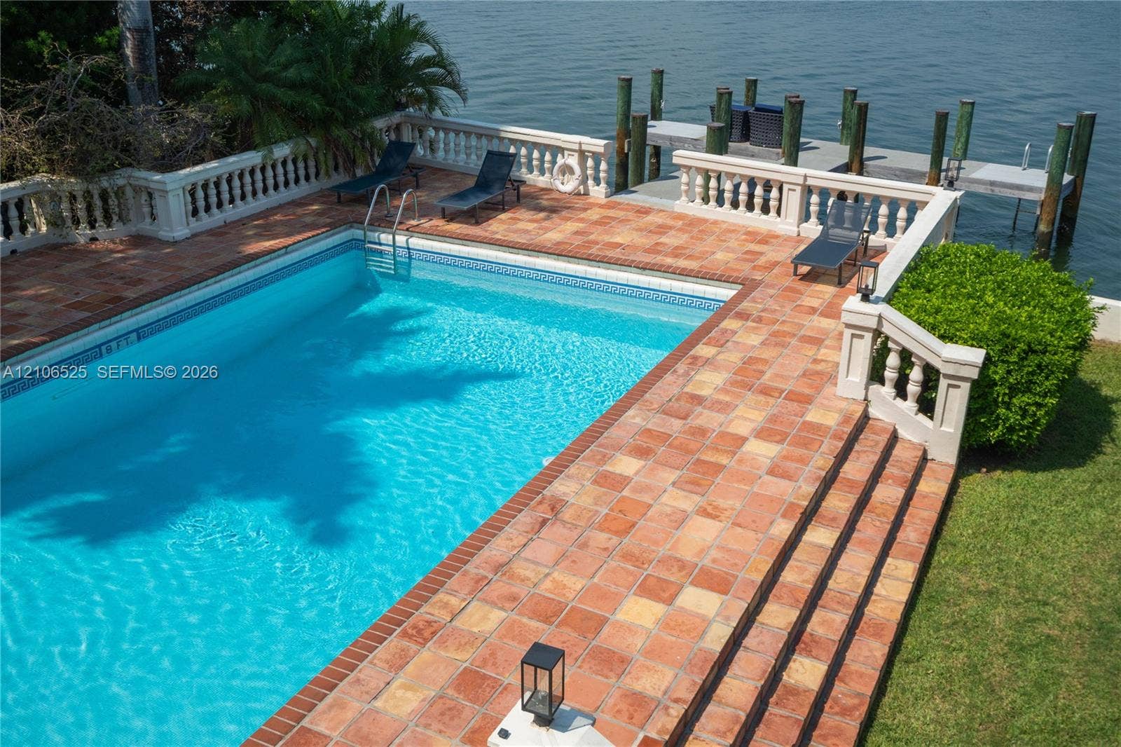 4760 N Bay Road, Miami Beach, FL 33140 In-ground swimming pool featuring a terra-cotta tile deck, a balustrade perimeter railing, and a private wooden dock extending over the water