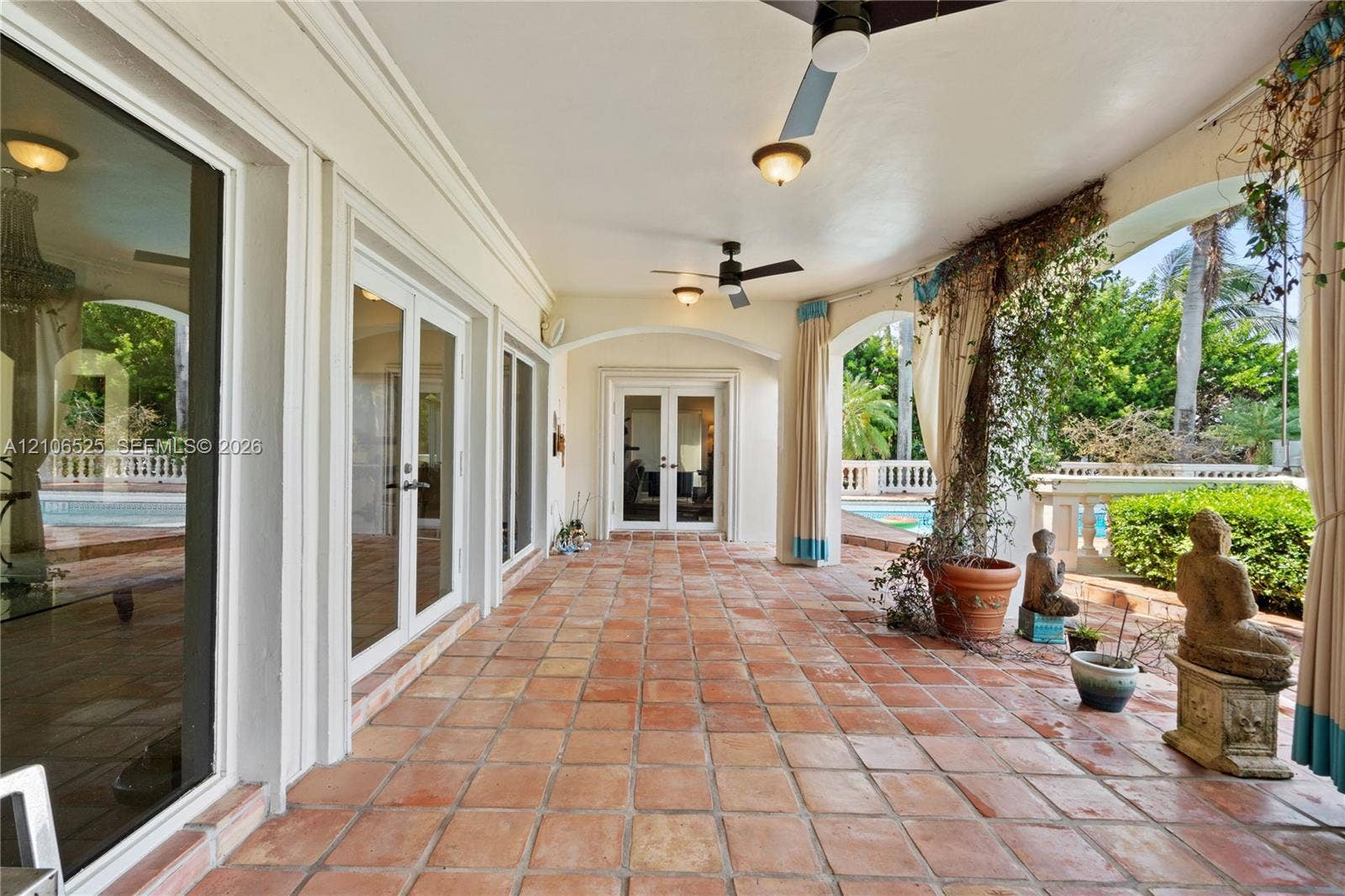 4760 N Bay Road, Miami Beach, FL 33140 Covered terrace featuring terra cotta tile flooring, multiple sets of glass French doors, arched architectural detailing, and ceiling-mounted fans