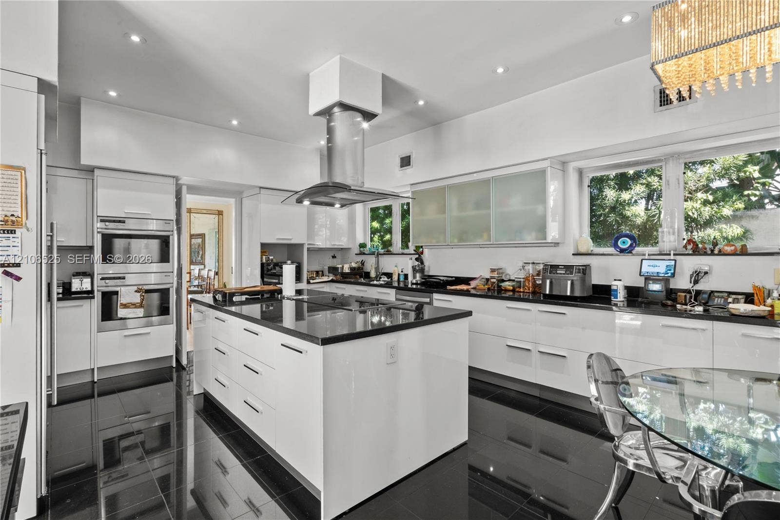 4760 N Bay Road, Miami Beach, FL 33140 Modern kitchen featuring high-gloss cabinetry, a central island with a stone-finish countertop, stainless steel double wall ovens, a ceiling-mounted stainless steel range hood, and polished tile flooring