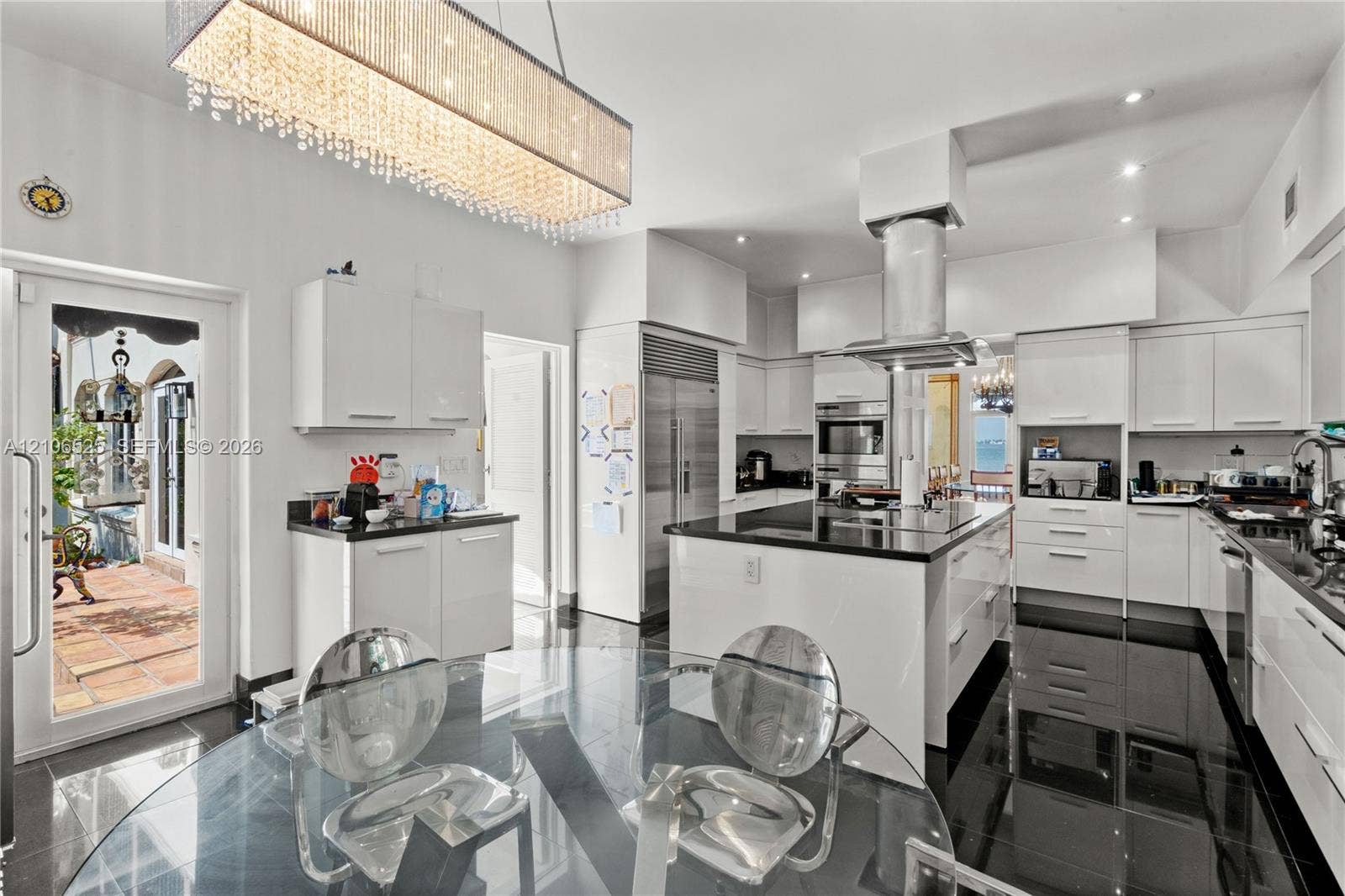 4760 N Bay Road, Miami Beach, FL 33140 Gourmet kitchen featuring high-gloss cabinetry, a central island with a stone countertop, stainless steel appliances, a cylindrical range hood, and a linear crystal chandelier