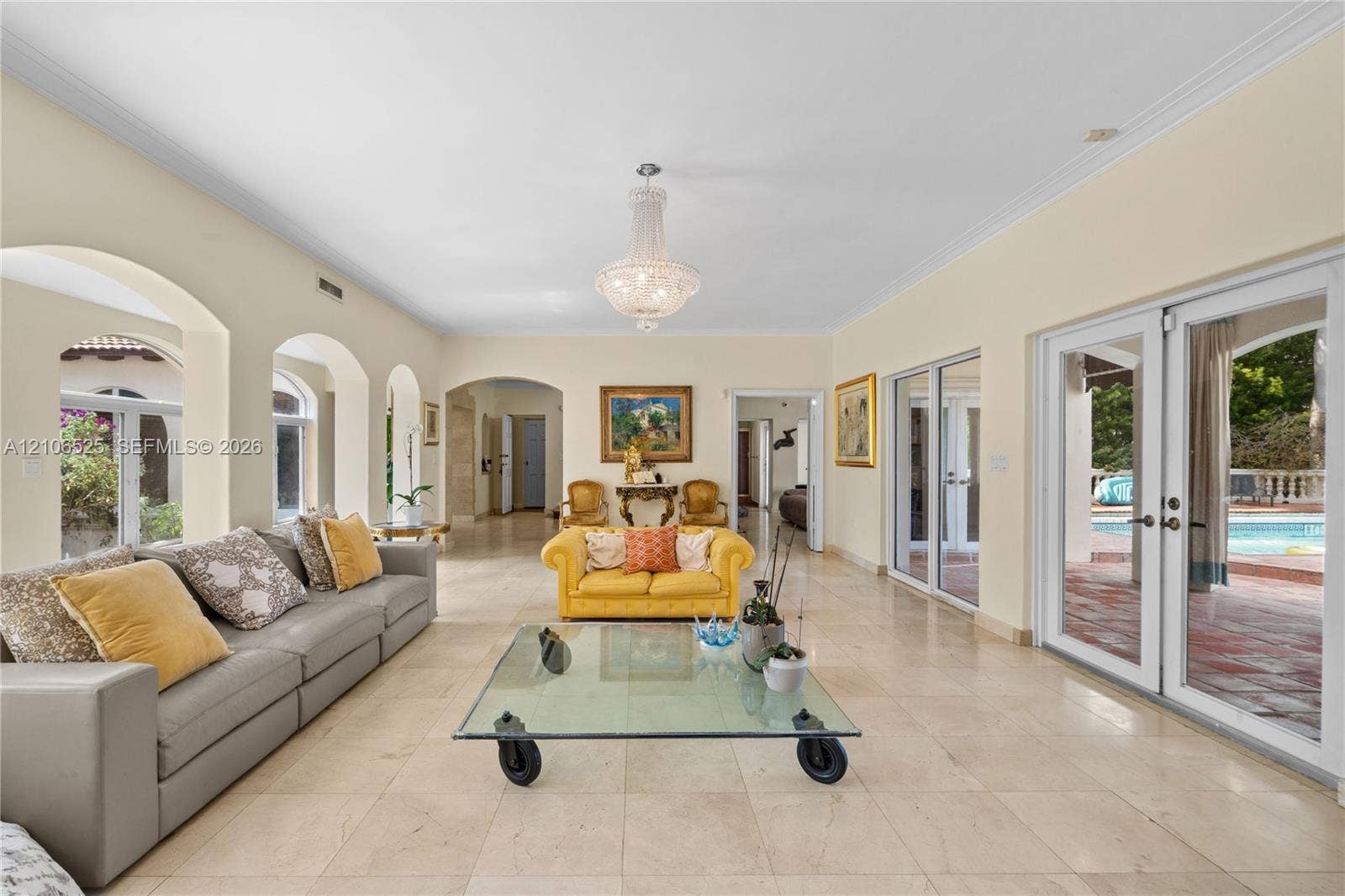 4760 N Bay Road, Miami Beach, FL 33140 Spacious living area featuring polished stone flooring, arched architectural details, a central crystal chandelier, and two sets of glass-paned double doors